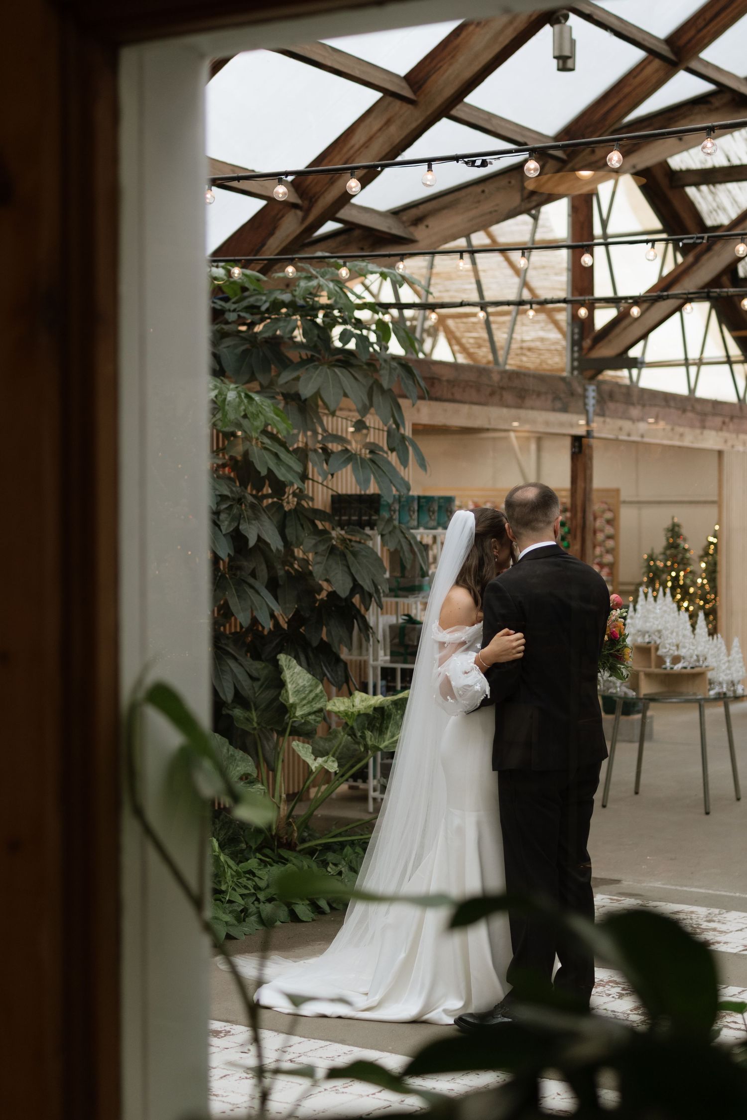 A romantic first dance between newlyweds in an elegant indoor venue with exposed wooden beams and string lights.