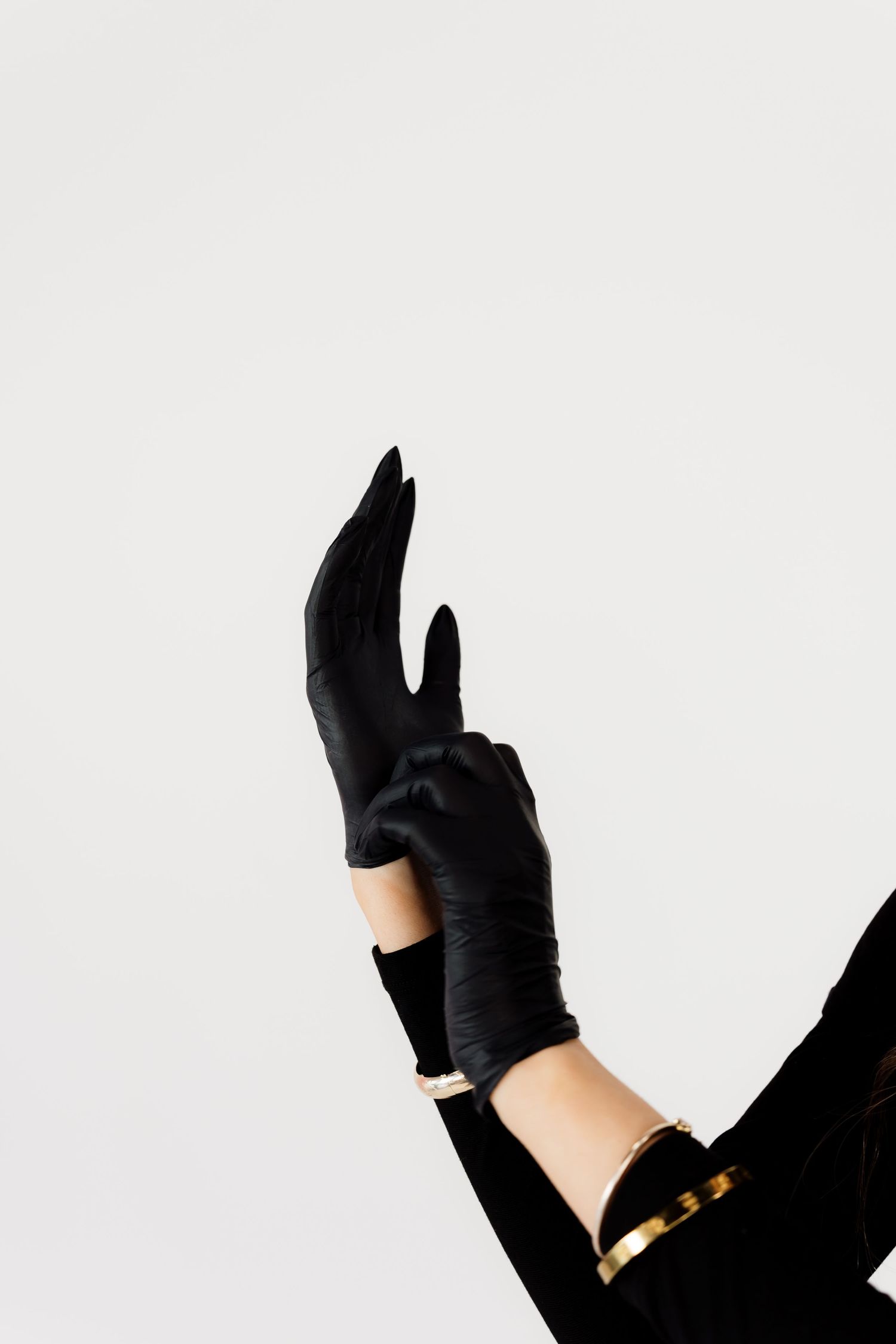 Hands wearing elegant black gloves with gold bracelet details against white background.