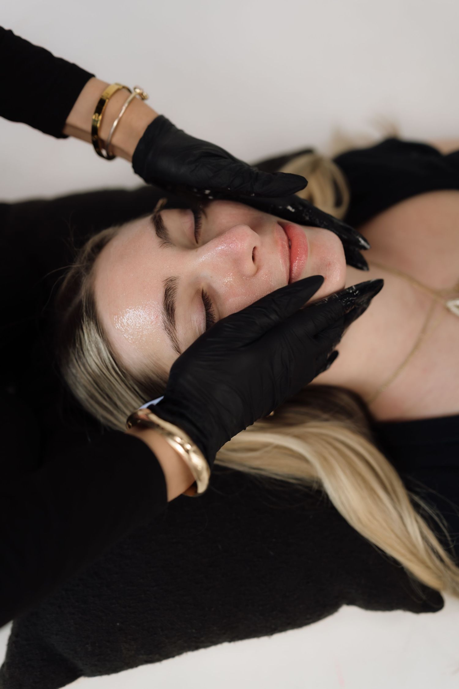 Aesthetic treatment being performed with black gloves on a relaxed client against white background.