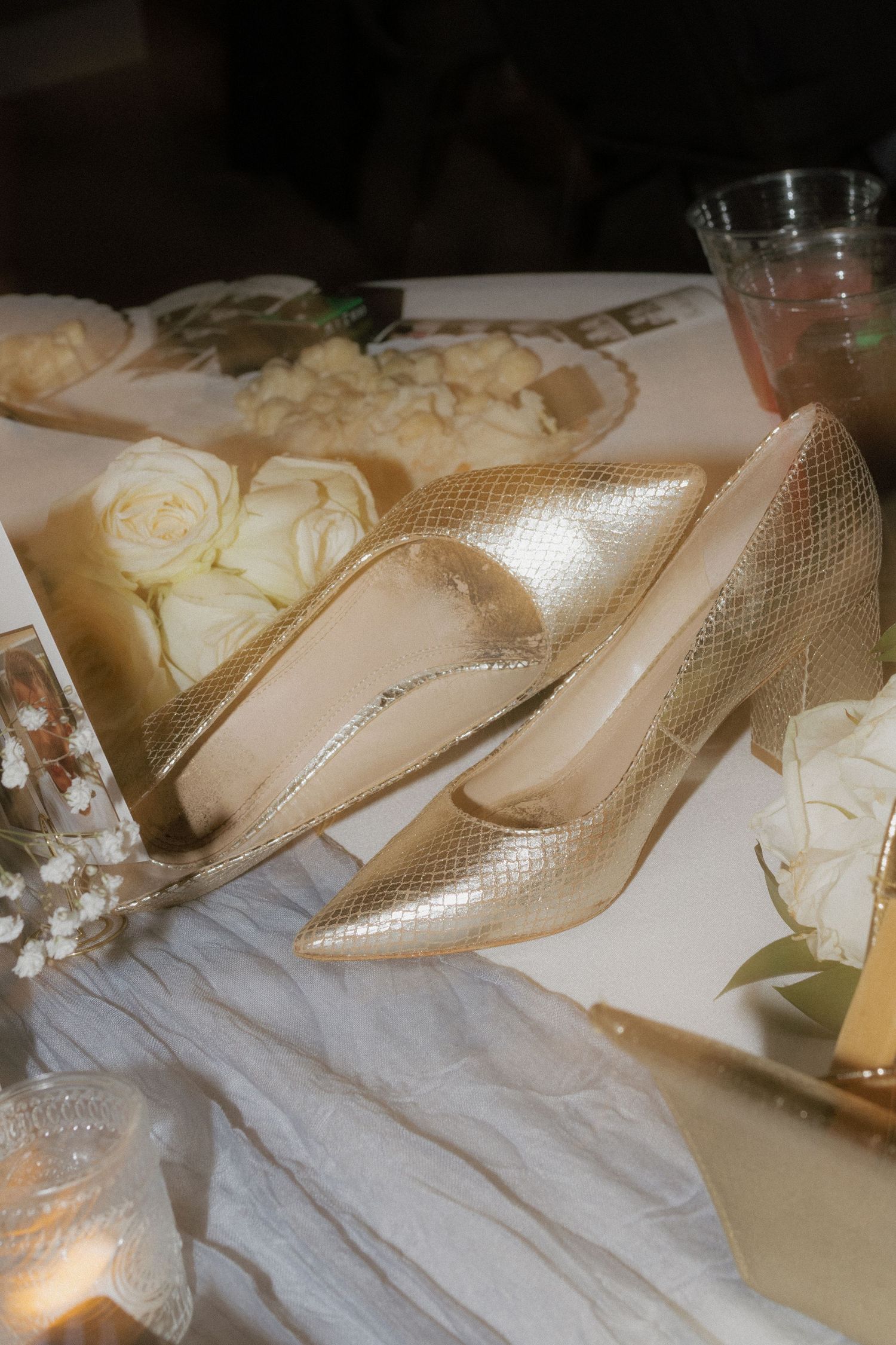 Elegant cream-colored bridal shoes displayed with floral decorations and white fabric.