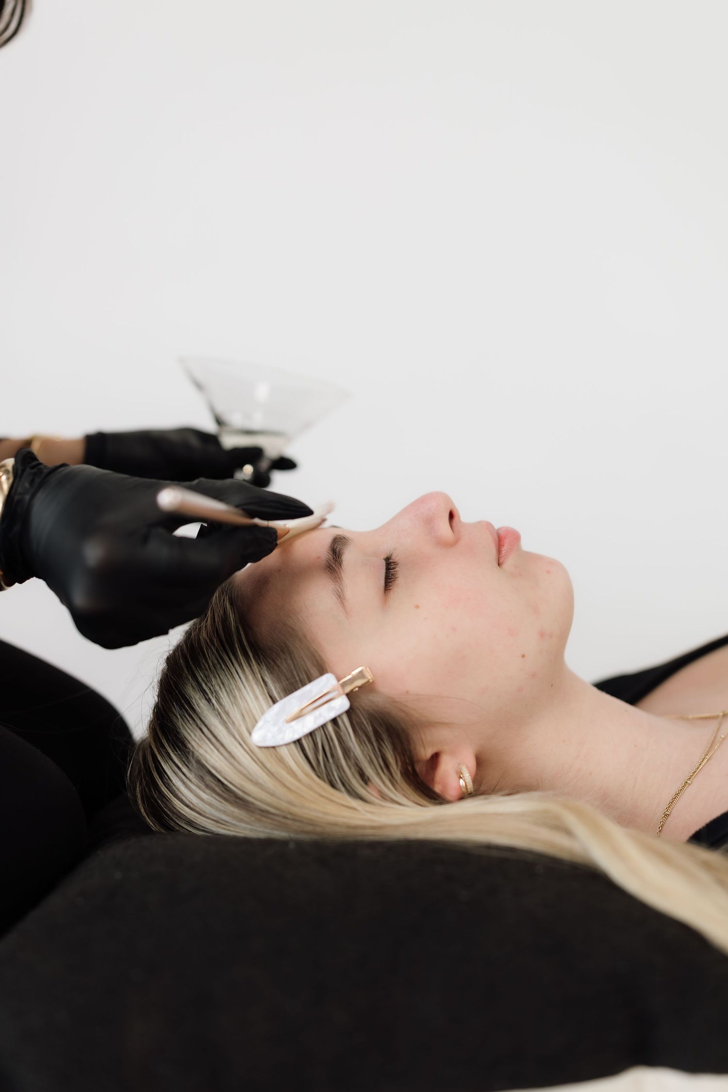 Close-up beauty shot showing black gloved hands performing a facial treatment on a reclining client.
