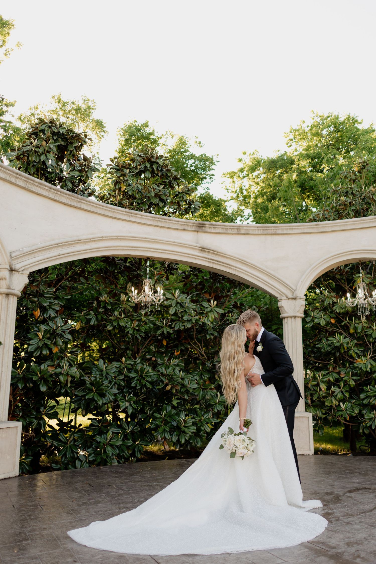 Wedding couple embracing under elegant white archways in an outdoor garden setting.