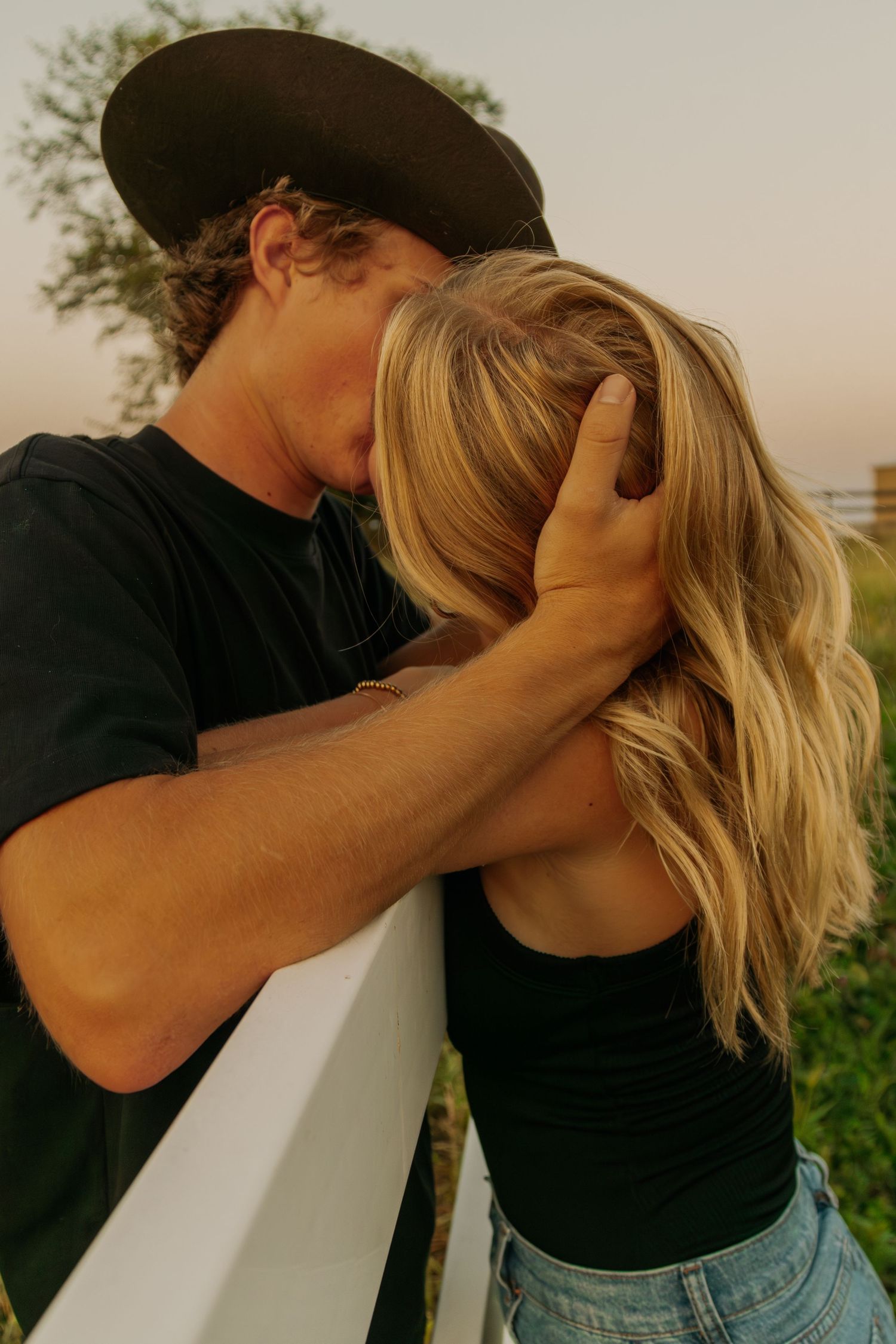 Two people in black shirts sharing a tender moment outdoors.