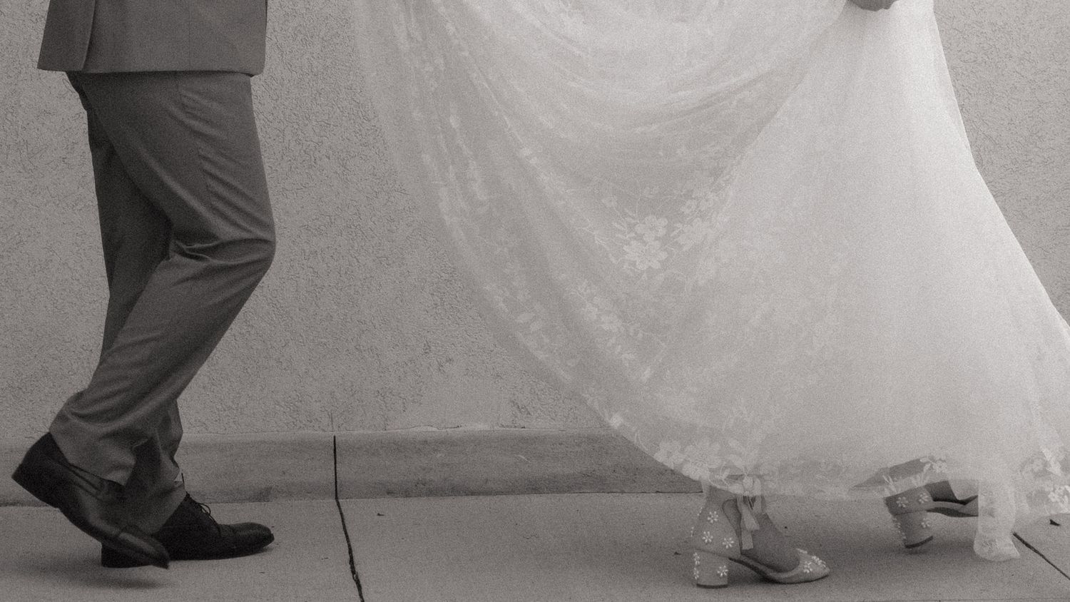 Close-up view of a white wedding dress and formal shoes during an outdoor celebration.