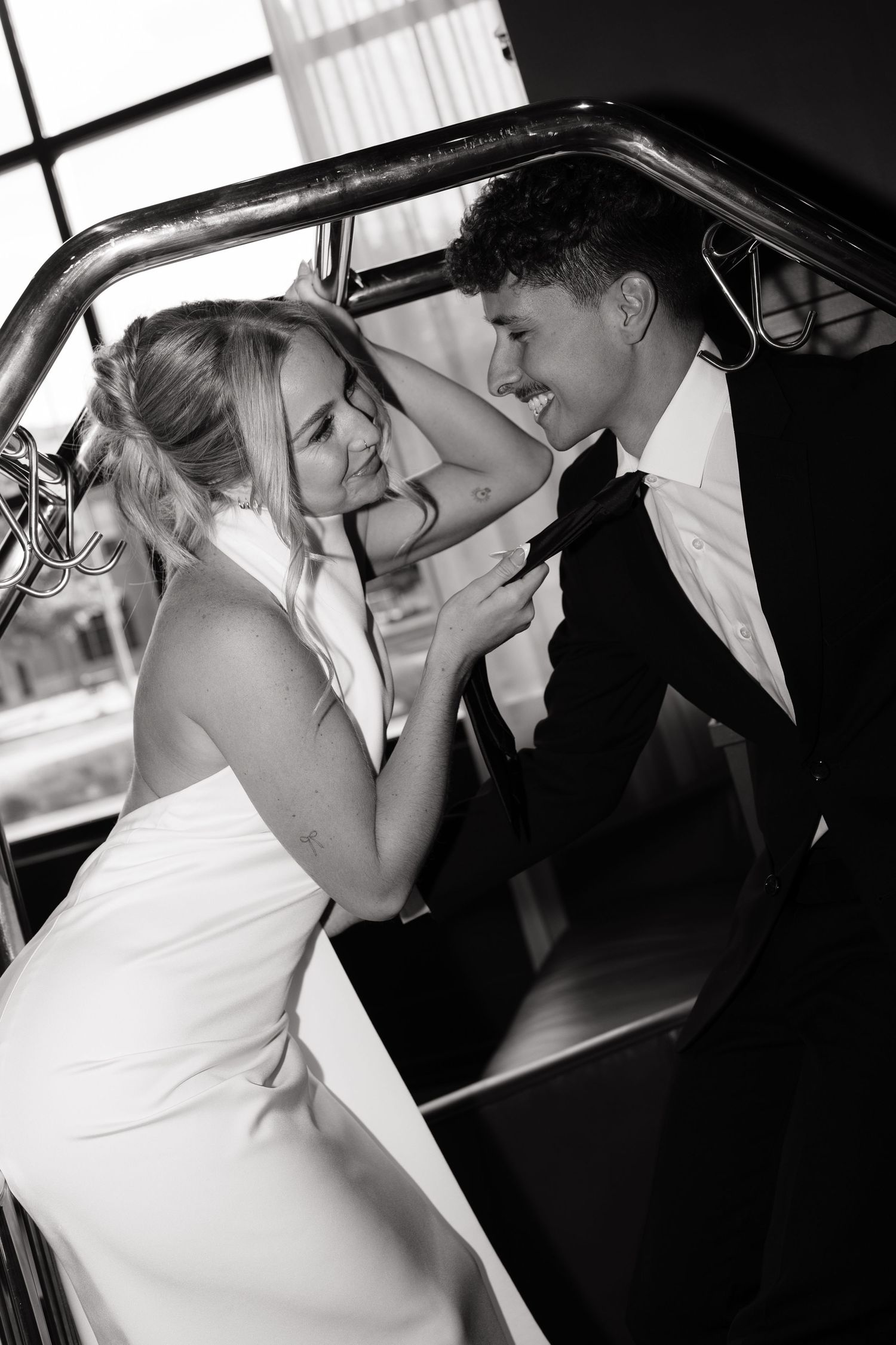 Black and white wedding photo of smiling bride and groom sharing a romantic moment on elegant staircase.
