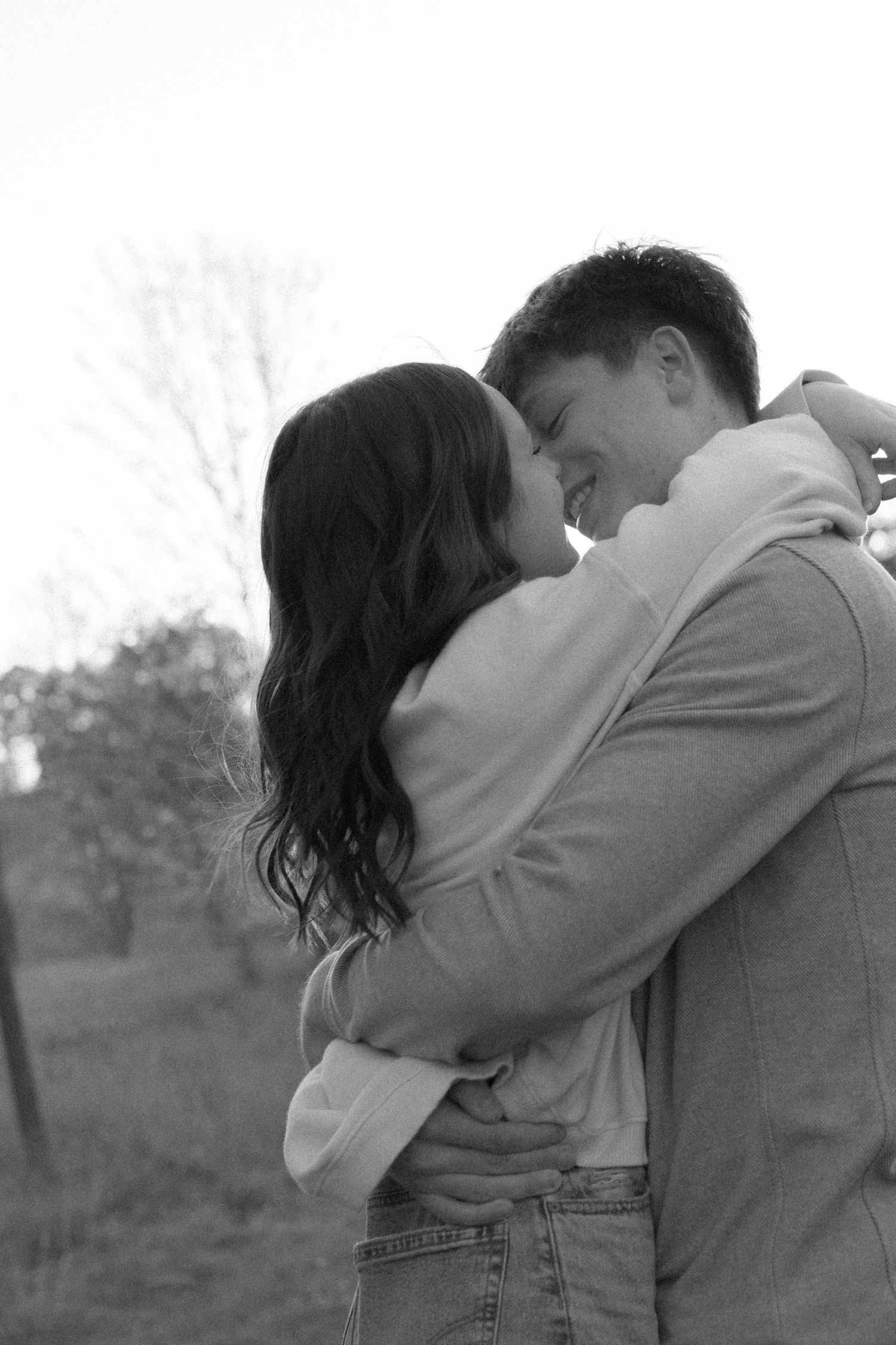 A tender black and white portrait of a couple embracing in an outdoor setting at sunset.