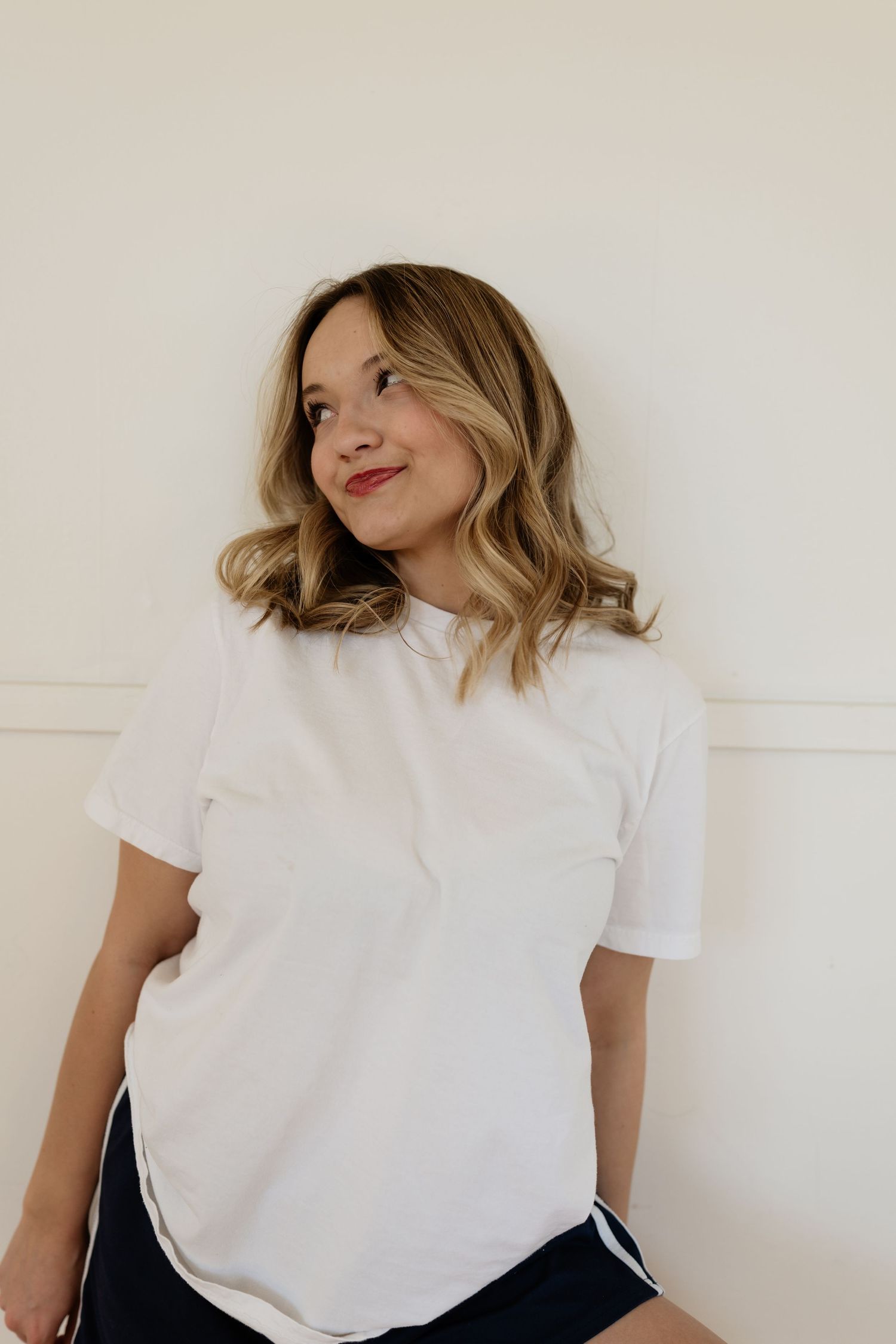 A person in a white t-shirt and dark pants poses in a casual sequence of lifestyle photos against a light wall.