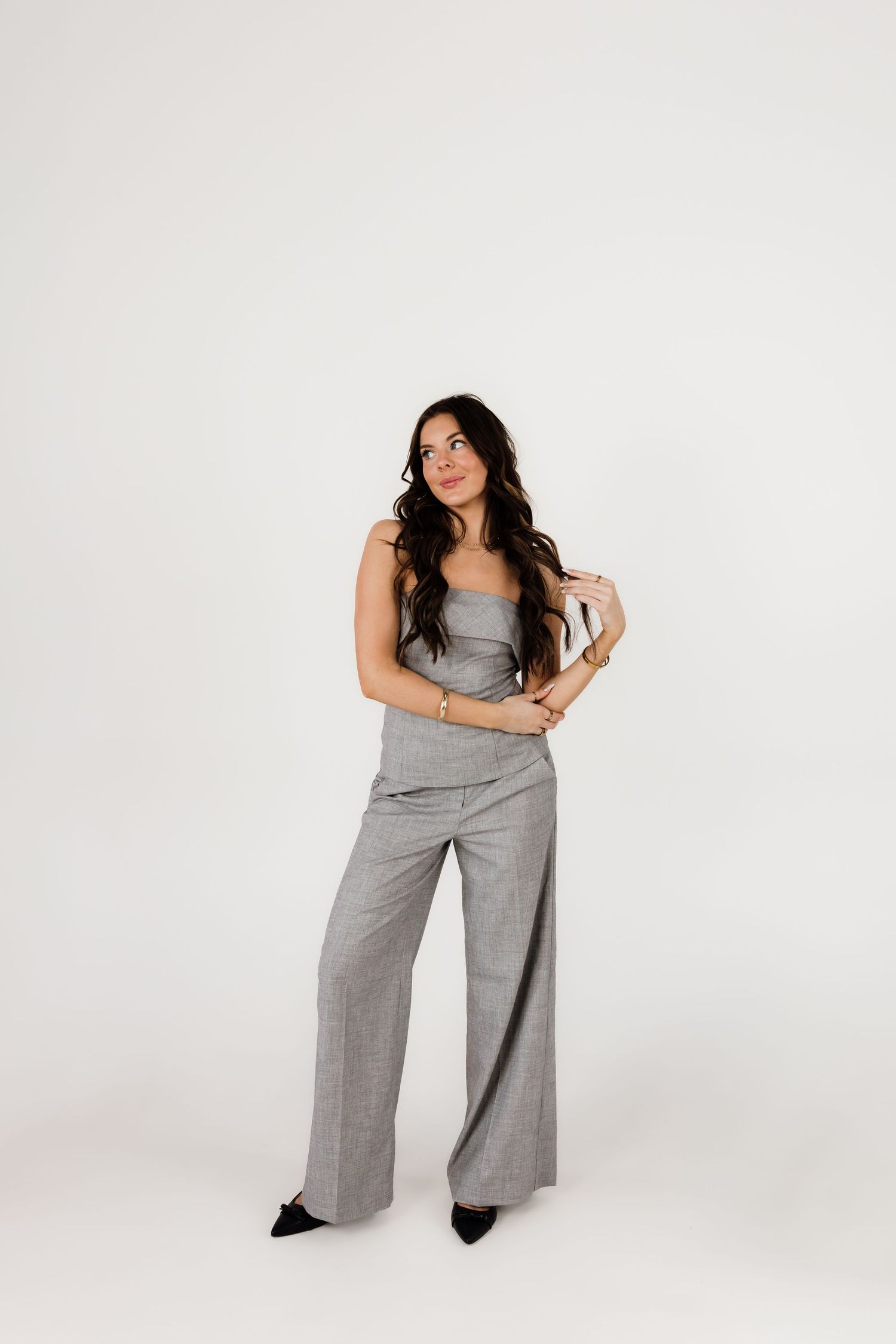 Woman wearing wide-leg gray jumpsuit poses confidently in studio setting.