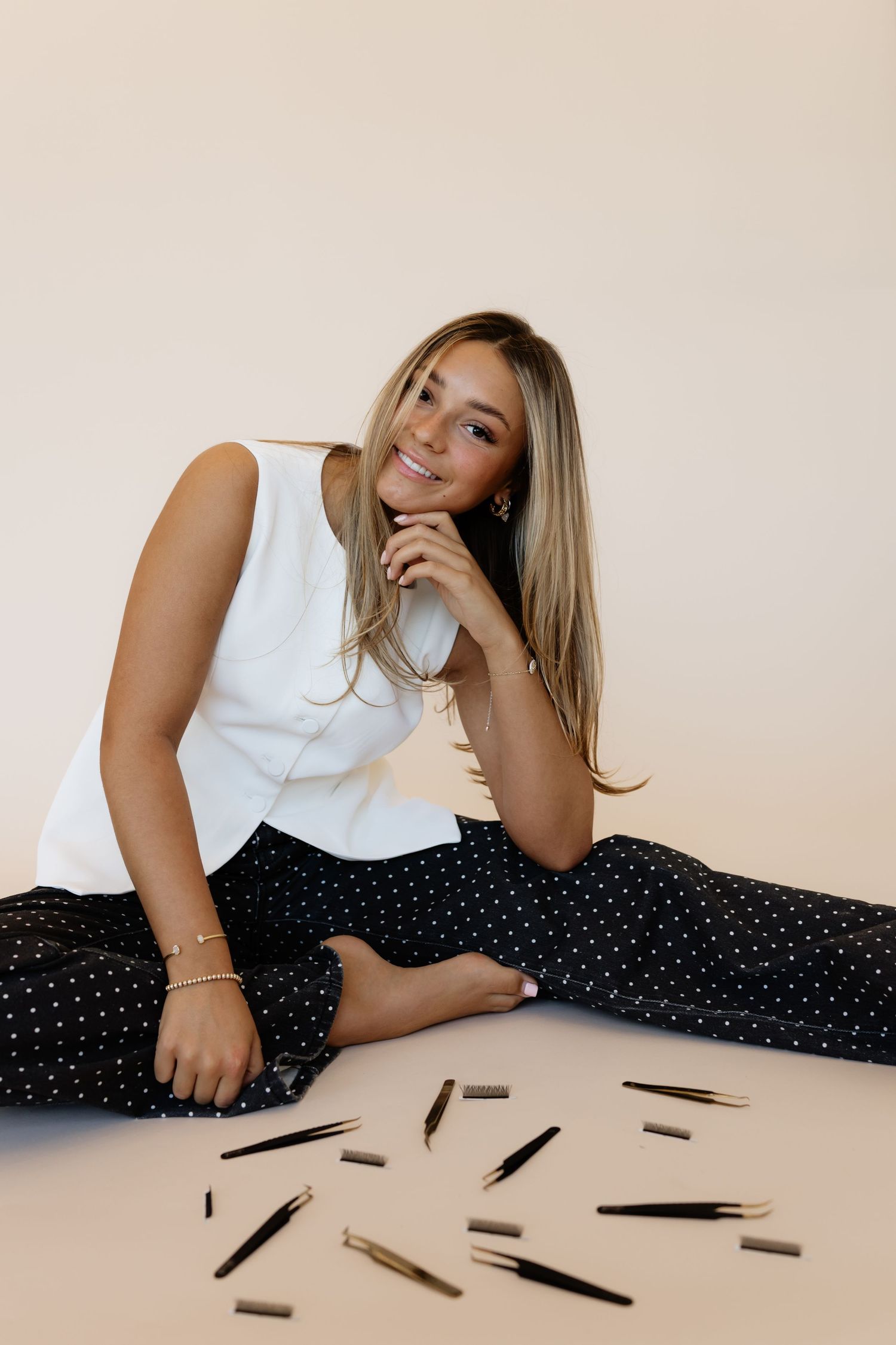 A person in a white top and polka dot skirt lies on a beige surface with scattered black pens around them.