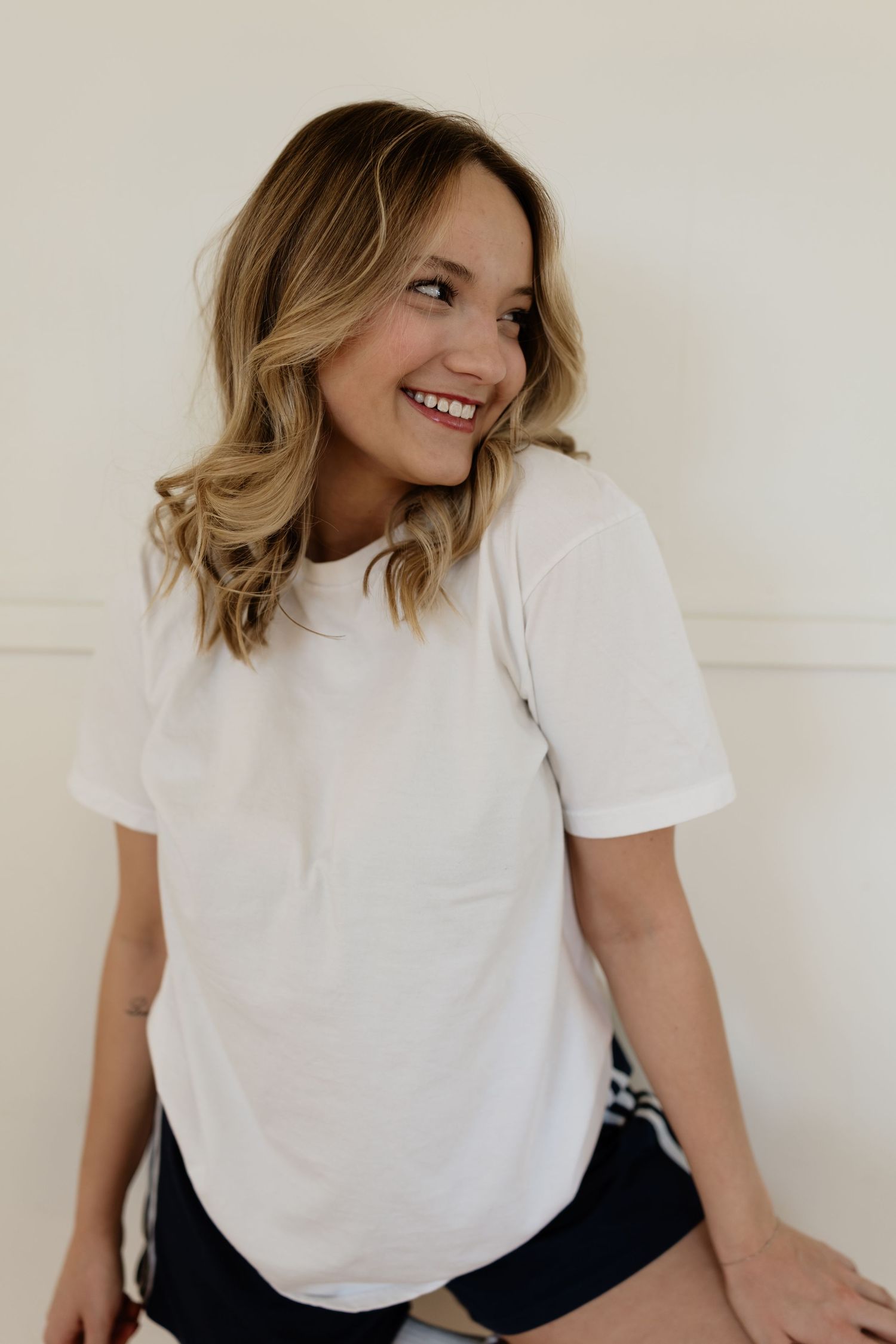 Side view portrait of a person in white t-shirt with blonde wavy hair smiling against light background.