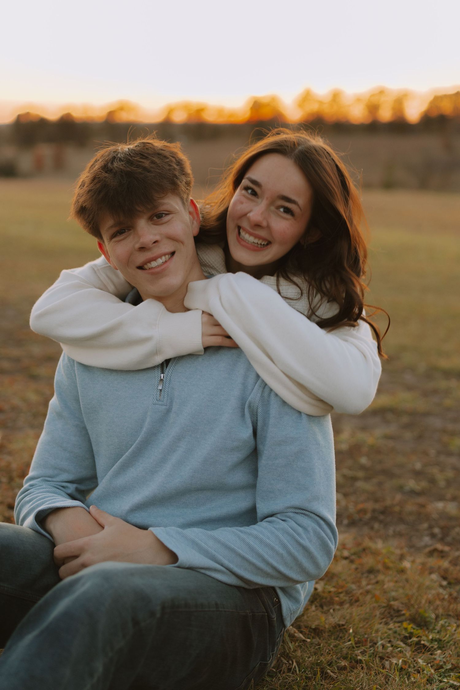 A playful couple in matching light blue and white sweaters sharing a joyful moment outdoors.