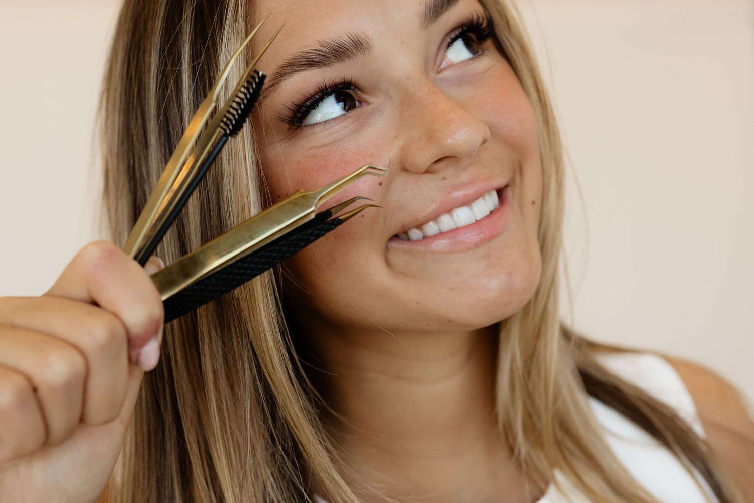 A person applies mascara to their eyelashes while smiling and looking upward in a series of beauty shots.