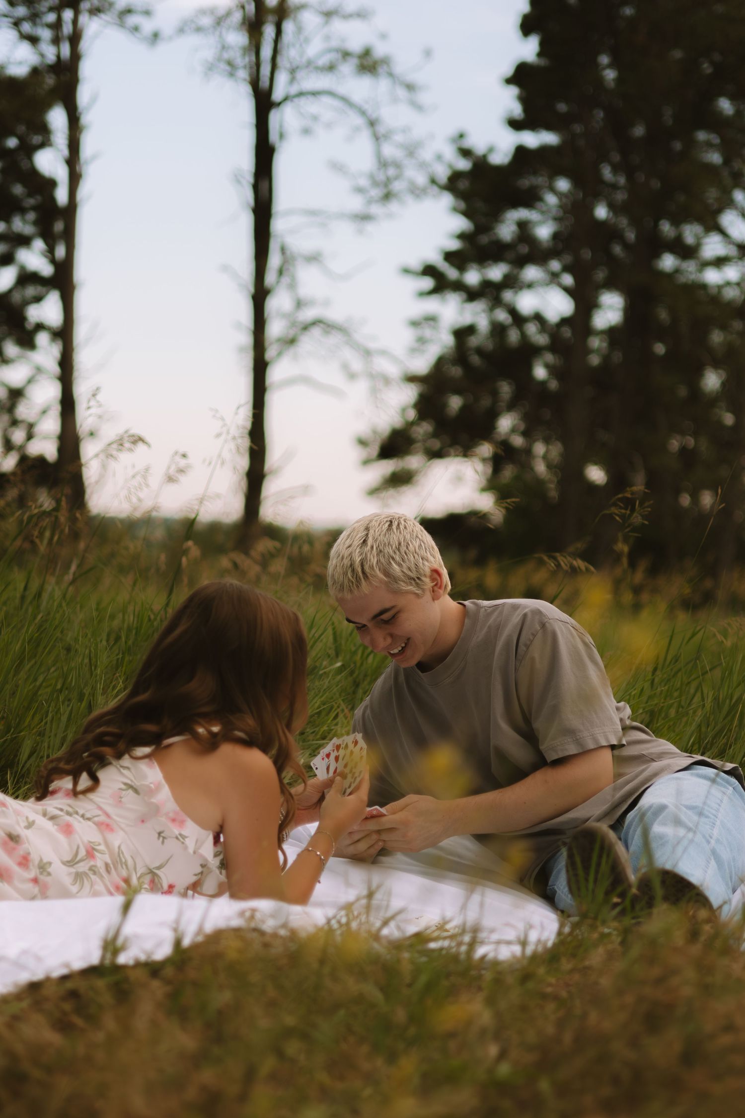 A couple lying on a white blanket in tall grass during a romantic outdoor photoshoot.