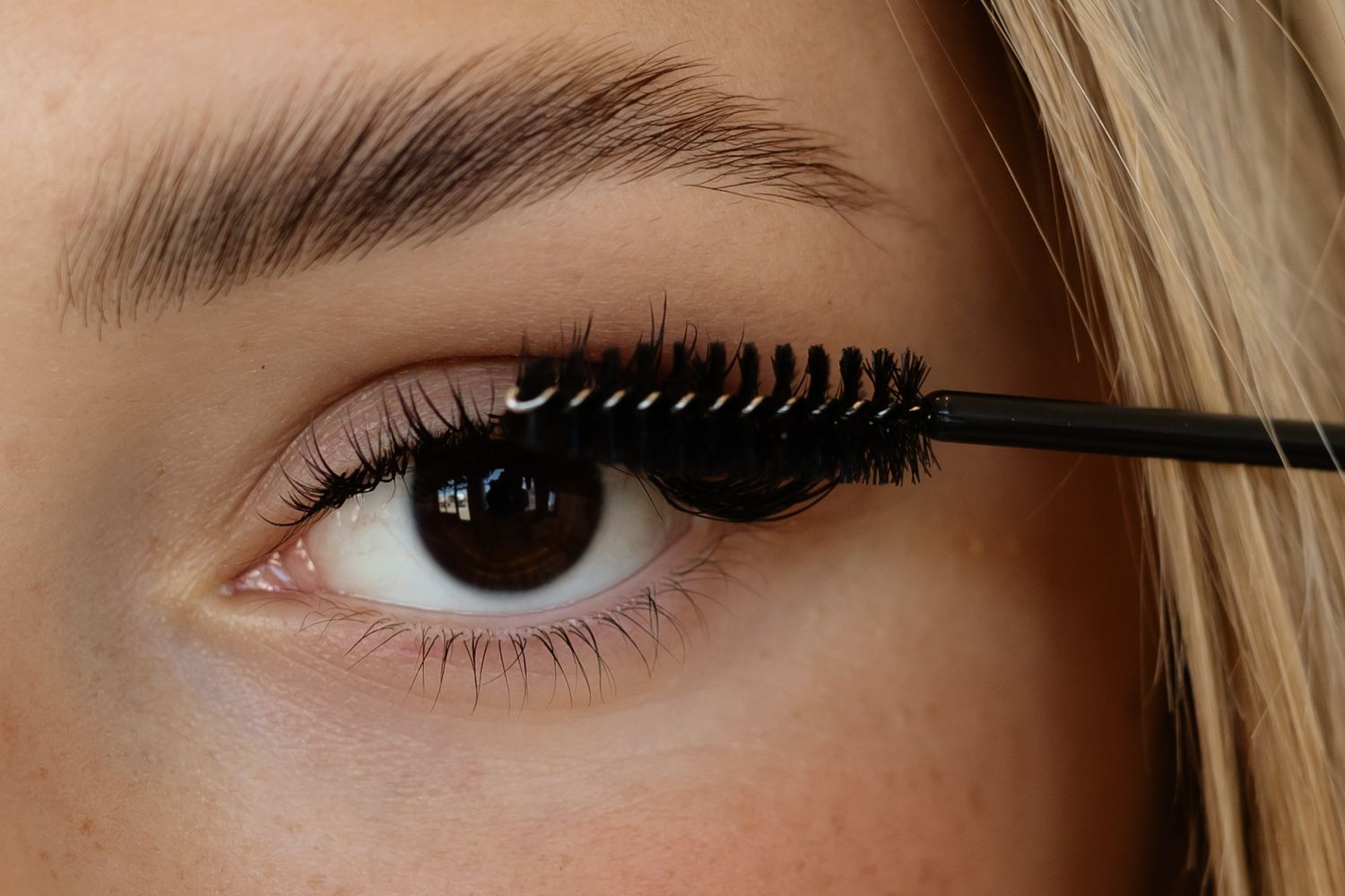 Close-up view of mascara being applied to eyelashes with a black brush wand.