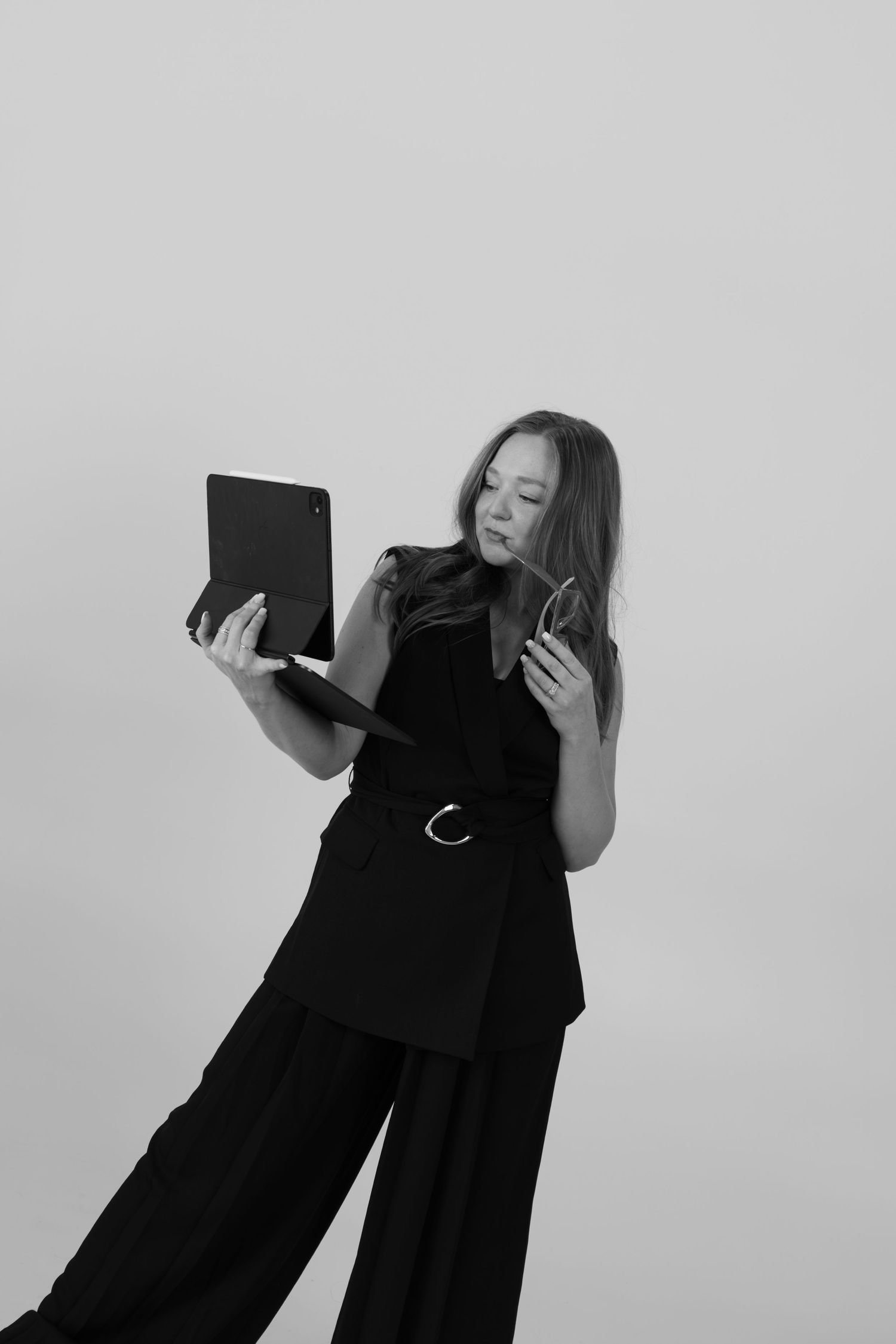 Professional in black outfit holds tablet while expressing animated gesture against light background.