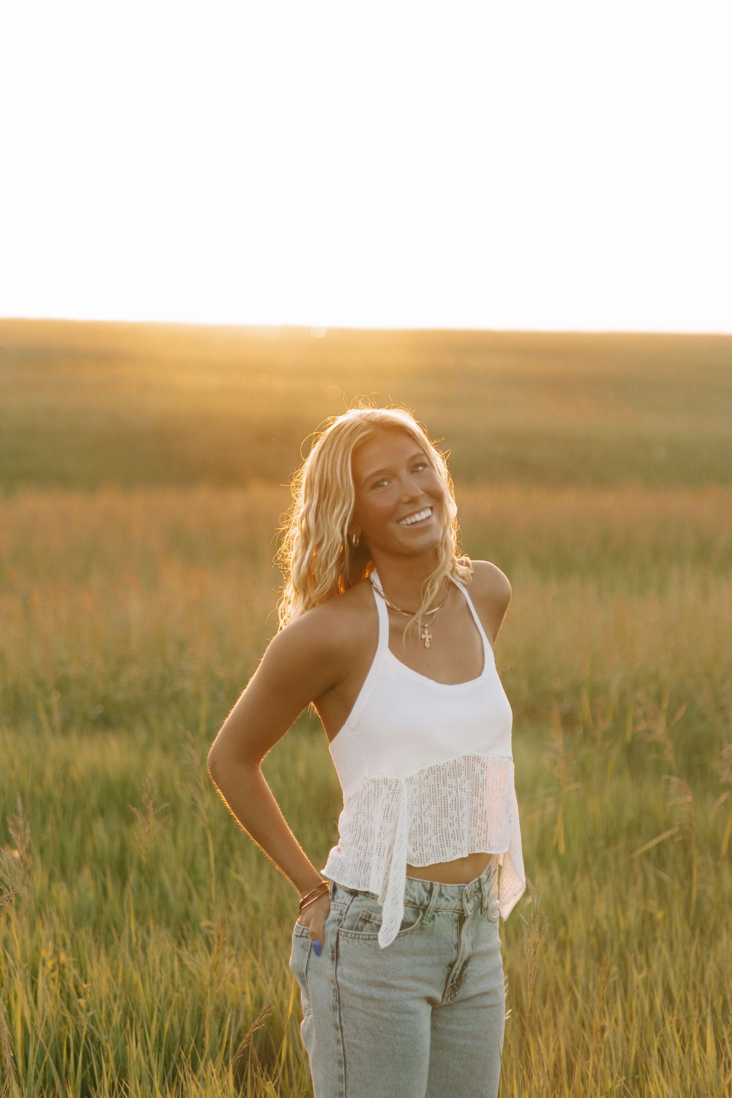Joyful summer fashion photography in a golden field wearing white lace top and denim.