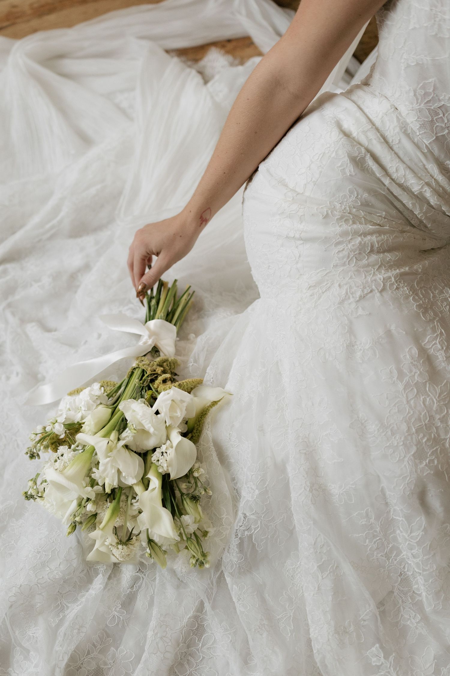 White bridal gown with delicate lace details and fresh white floral bouquet.