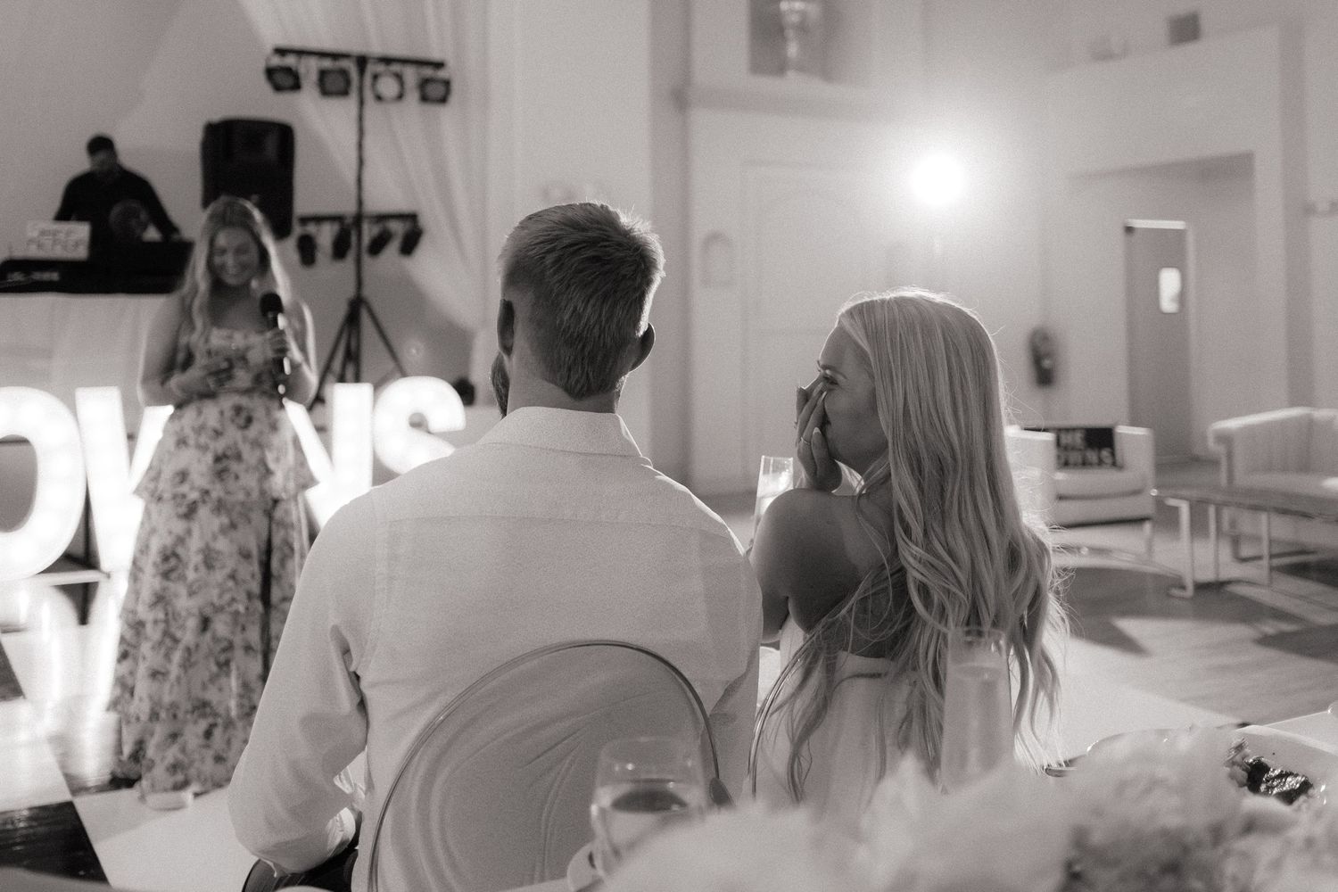 Black and white candid wedding reception scene with guests in an indoor venue.