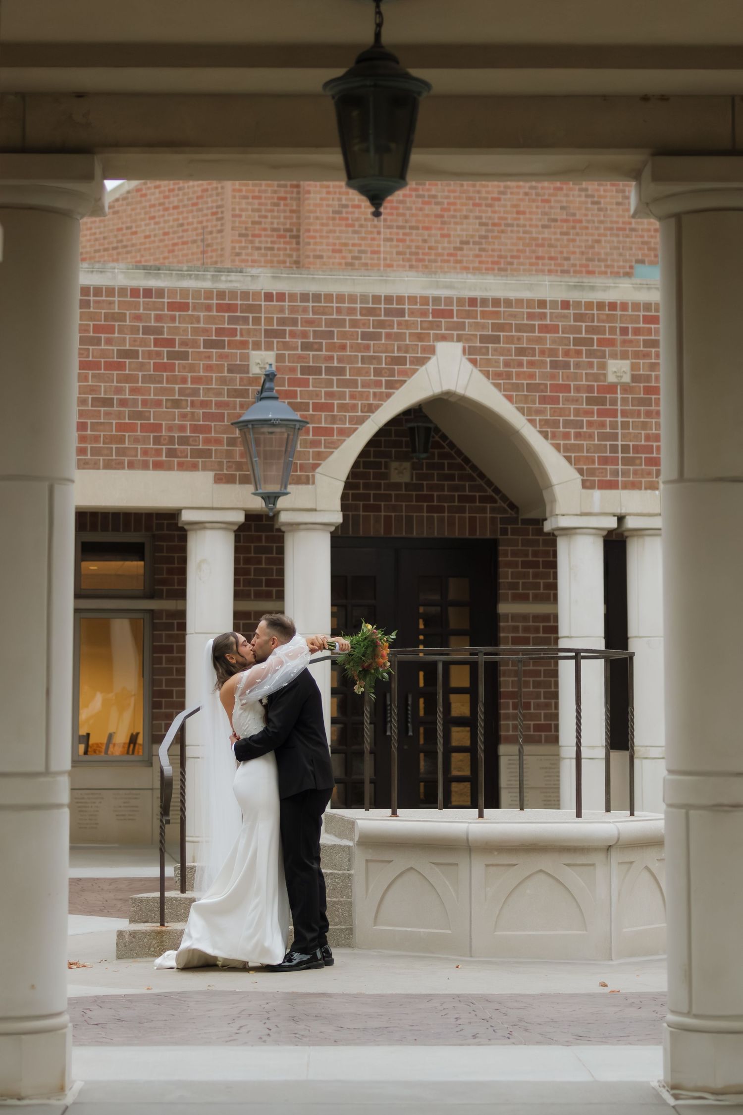 Romantic moment captured under brick archways with white columns at wedding venue.