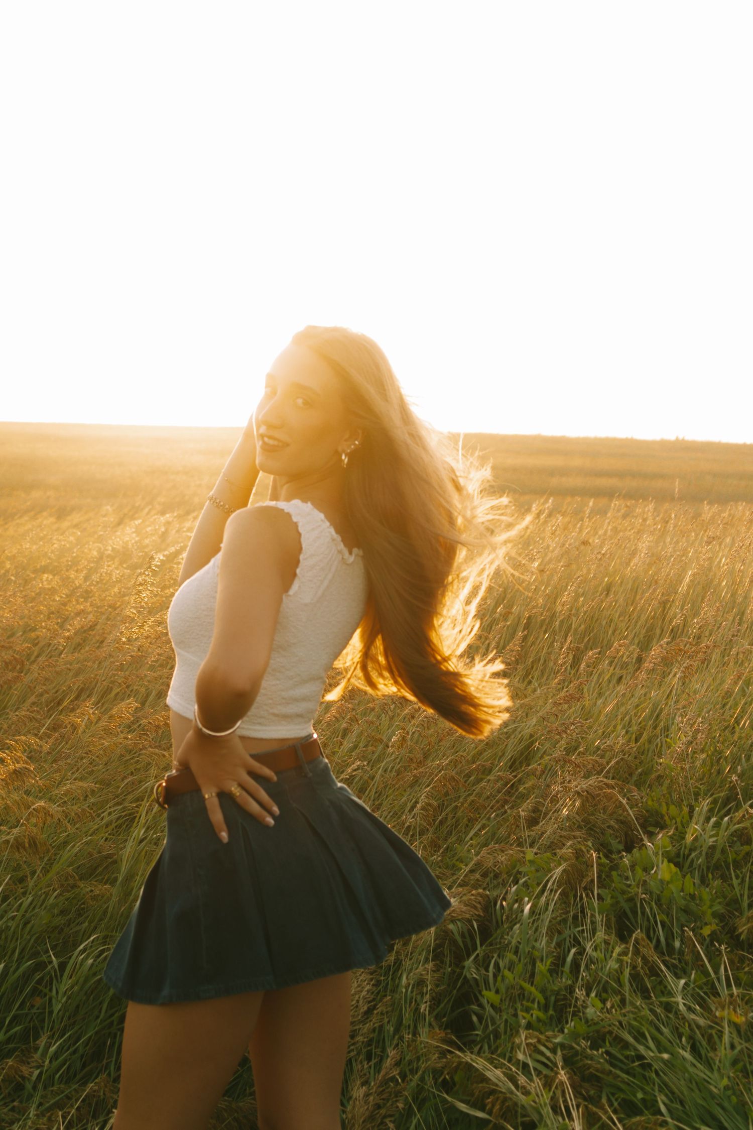 A person in a white top and dark skirt twirls in a golden field at sunset.