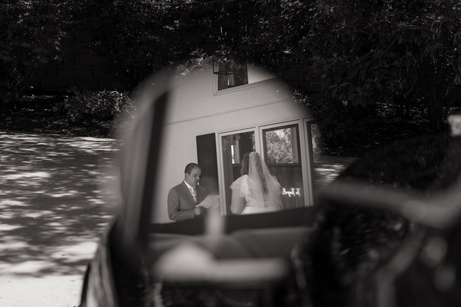 A black and white reflection in a car mirror shows a wedding moment.