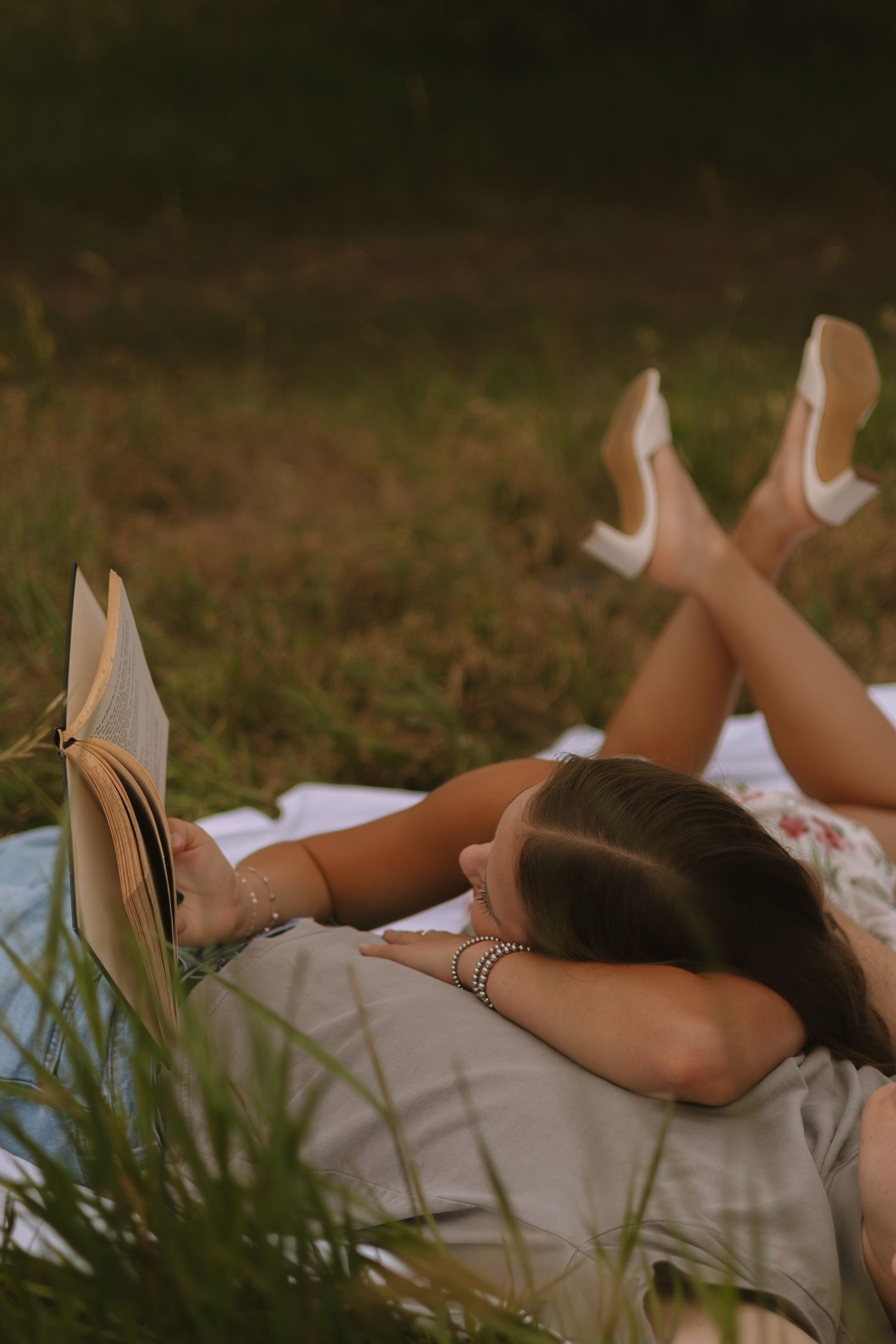 Woman relaxing on white blanket outdoors during golden hour photography session.