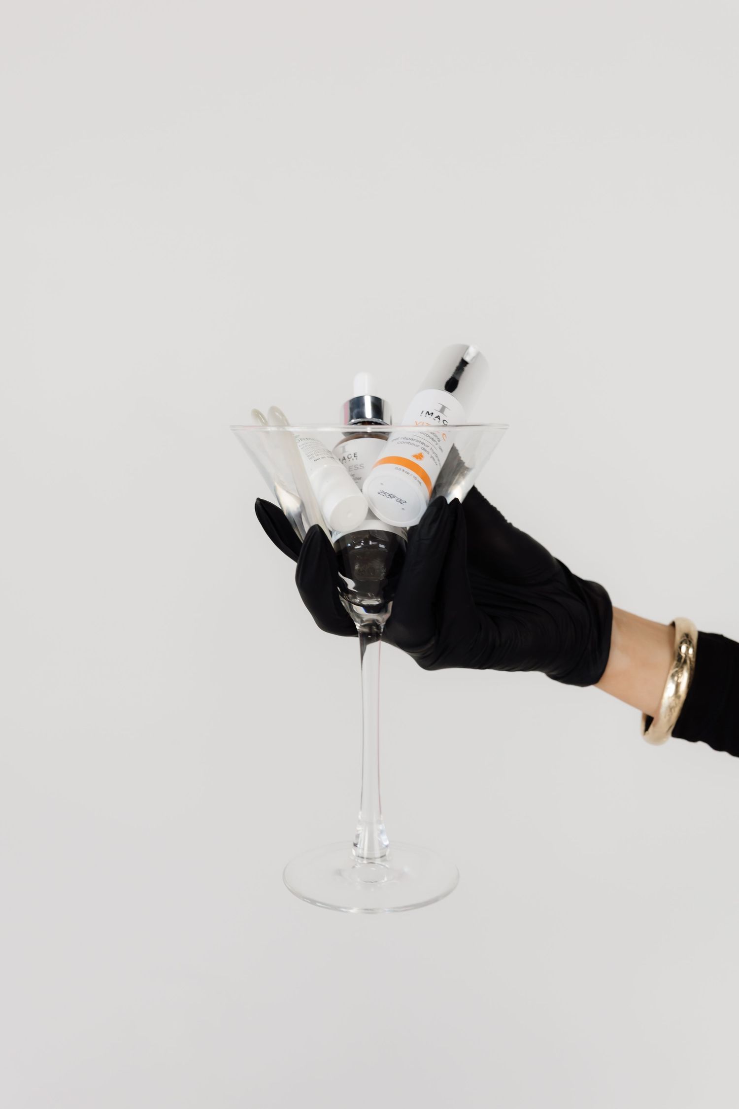 Hand in black glove holding martini glass against minimalist white backdrop.