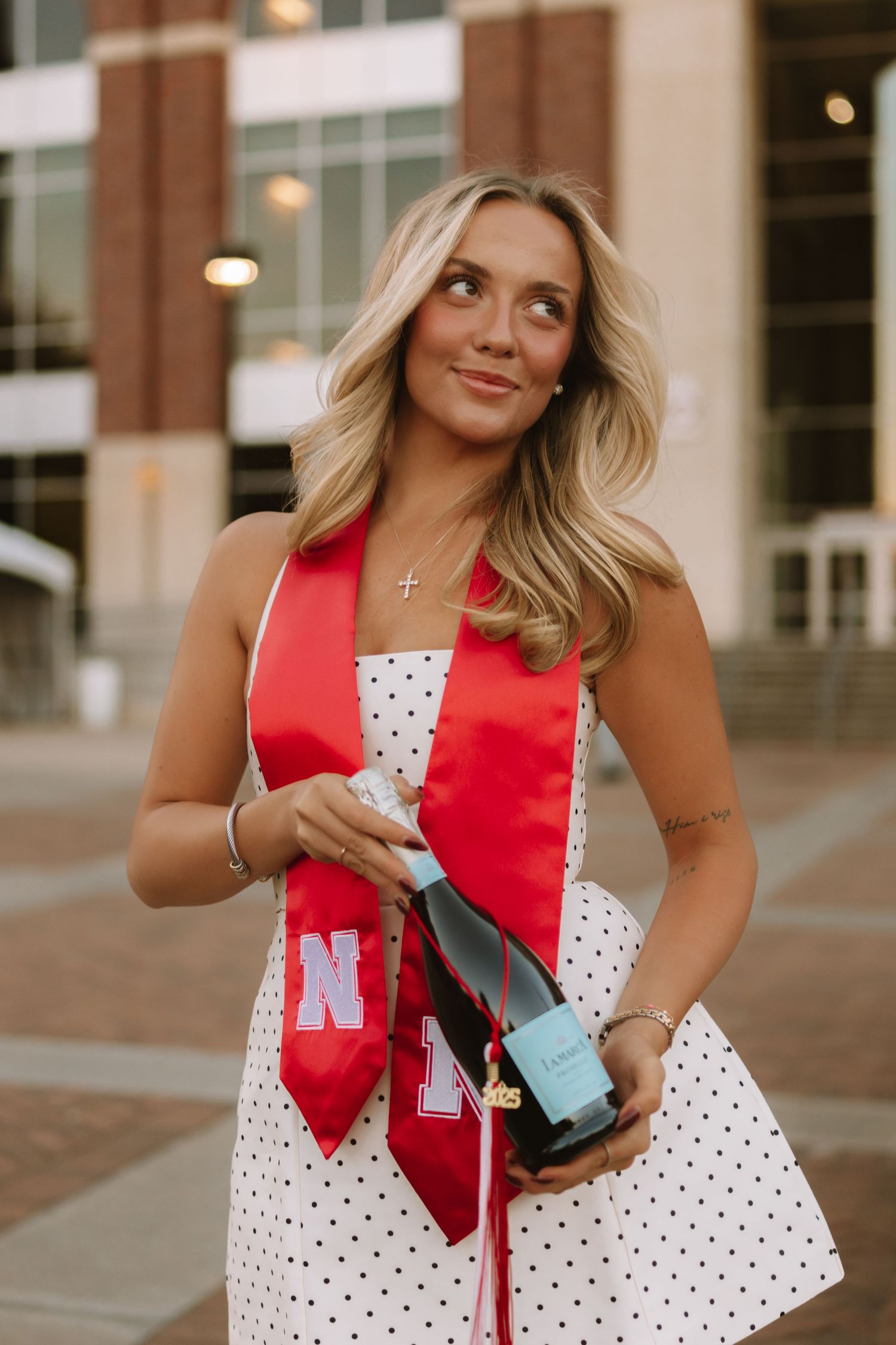 College graduate shows off diploma and red graduation stole with university logos.