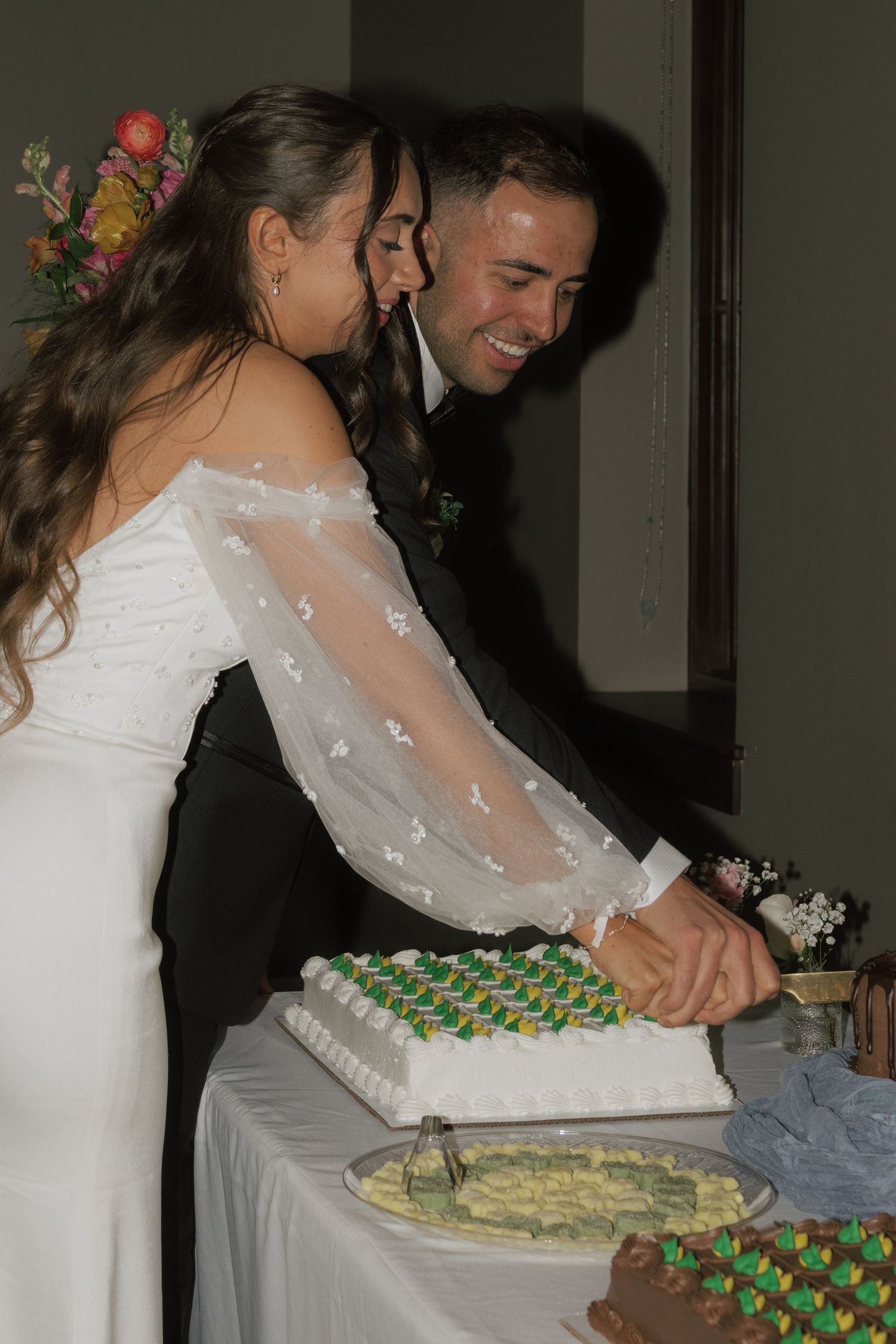 Couple cutting their wedding cake decorated with green frosting details.