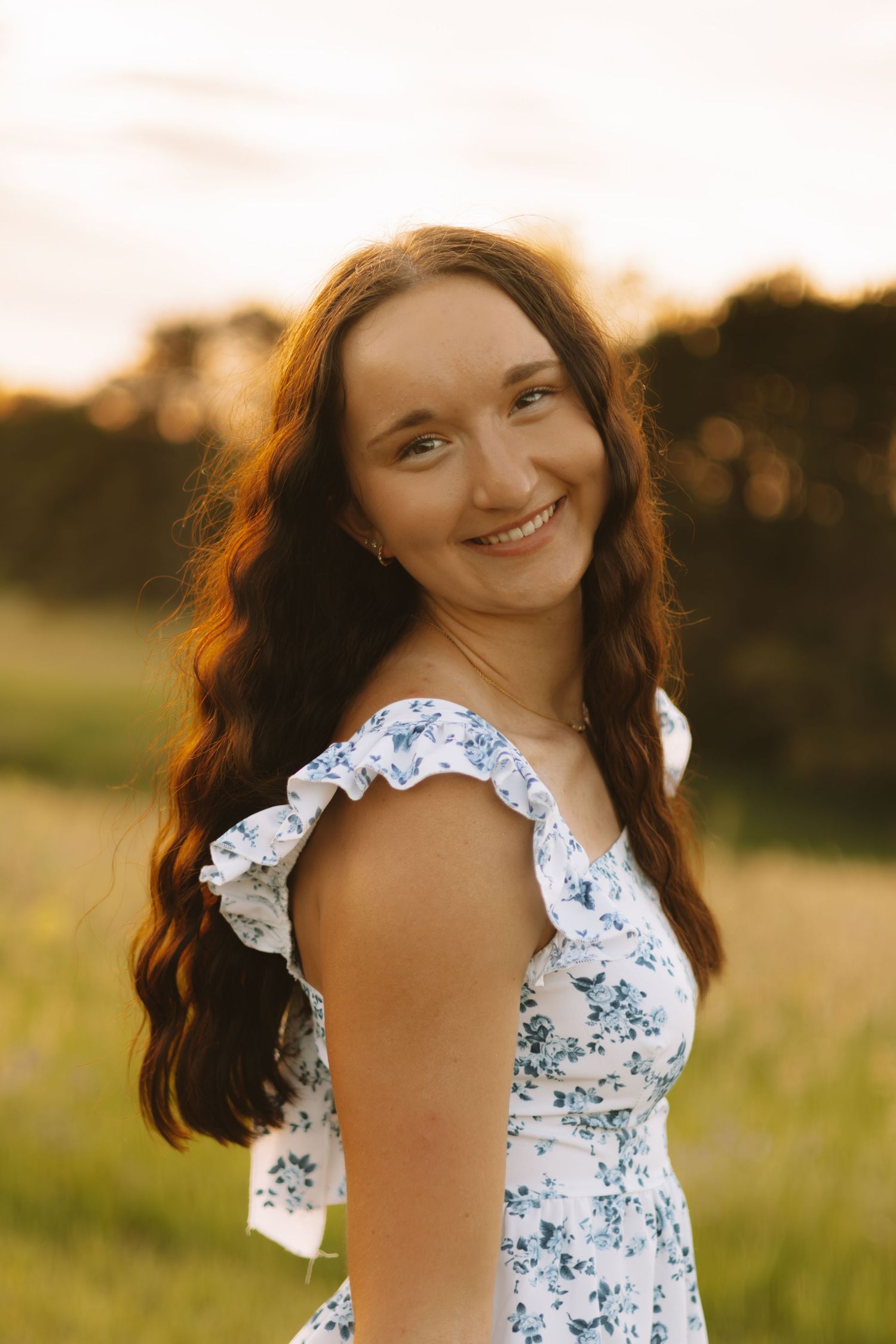 Summer portrait in a floral dress with ruffled sleeves during golden hour in a meadow.