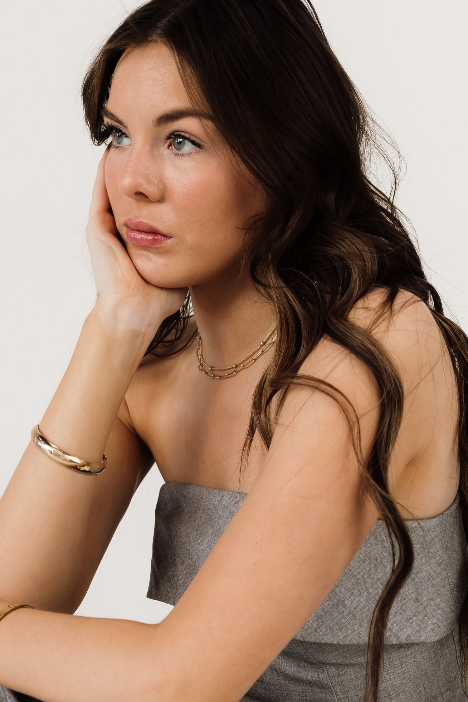 Fashion model in grey top poses elegantly against white backdrop.