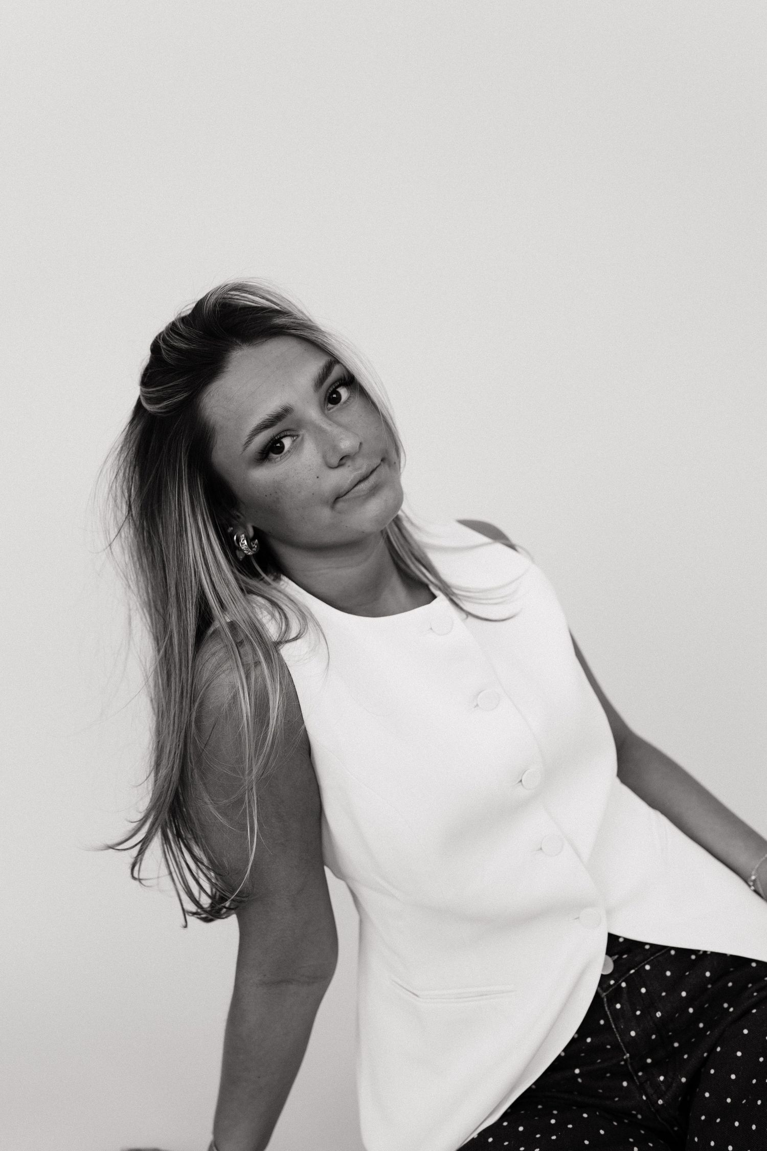 A series of black and white photos showing a person in a white sleeveless top and polka dot skirt posing against a wall.