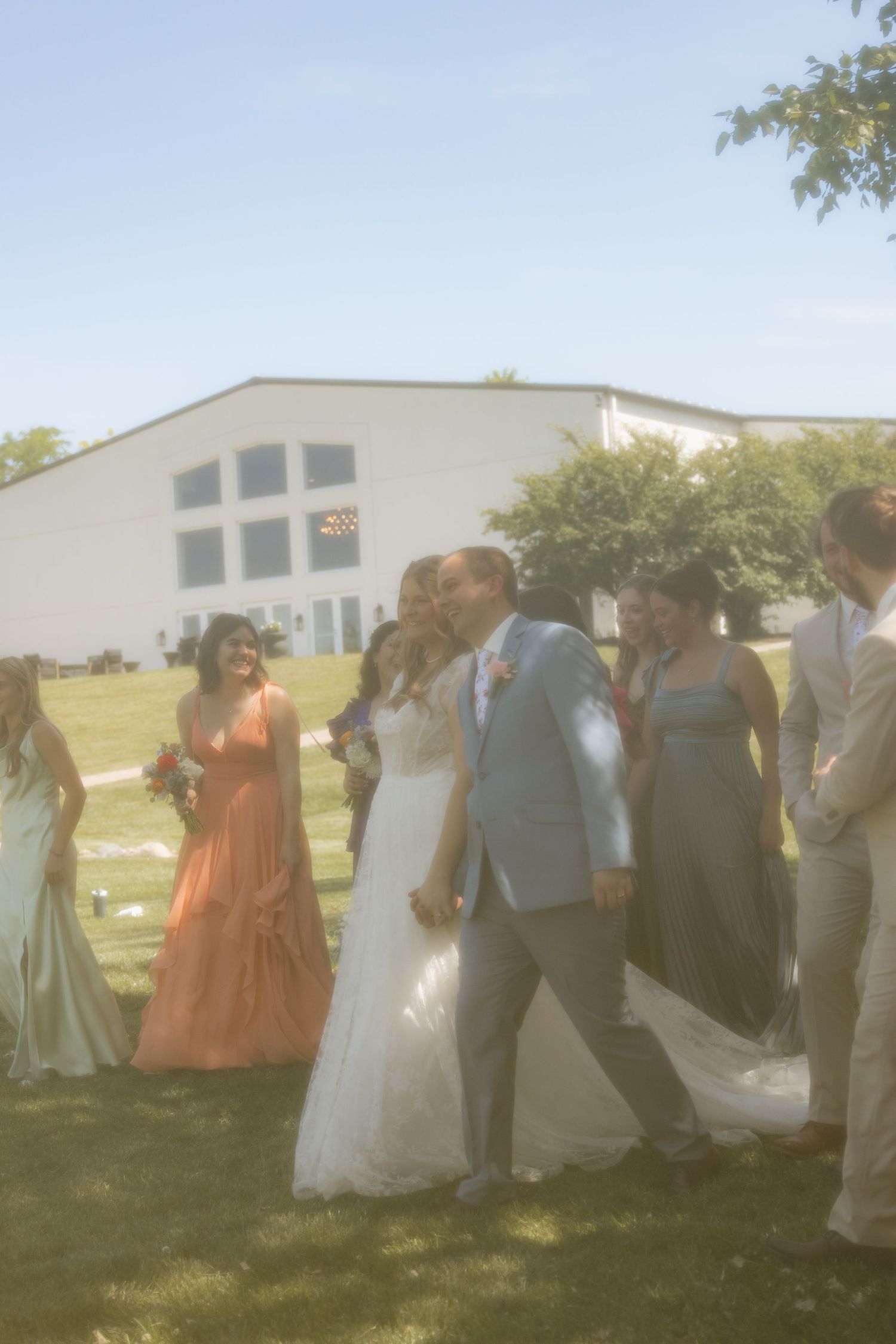 Wedding party members in colorful dresses gather outdoors on a sunny day for group photos.