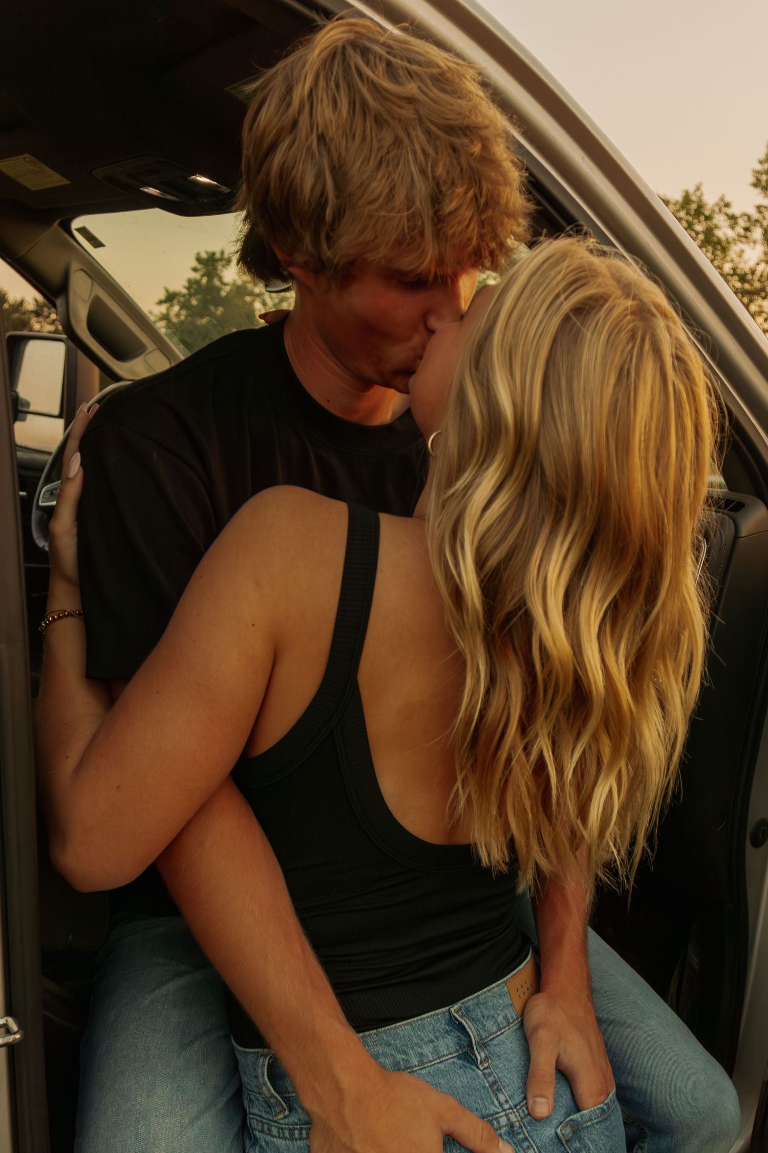 A couple in casual attire sharing an intimate moment near a car.