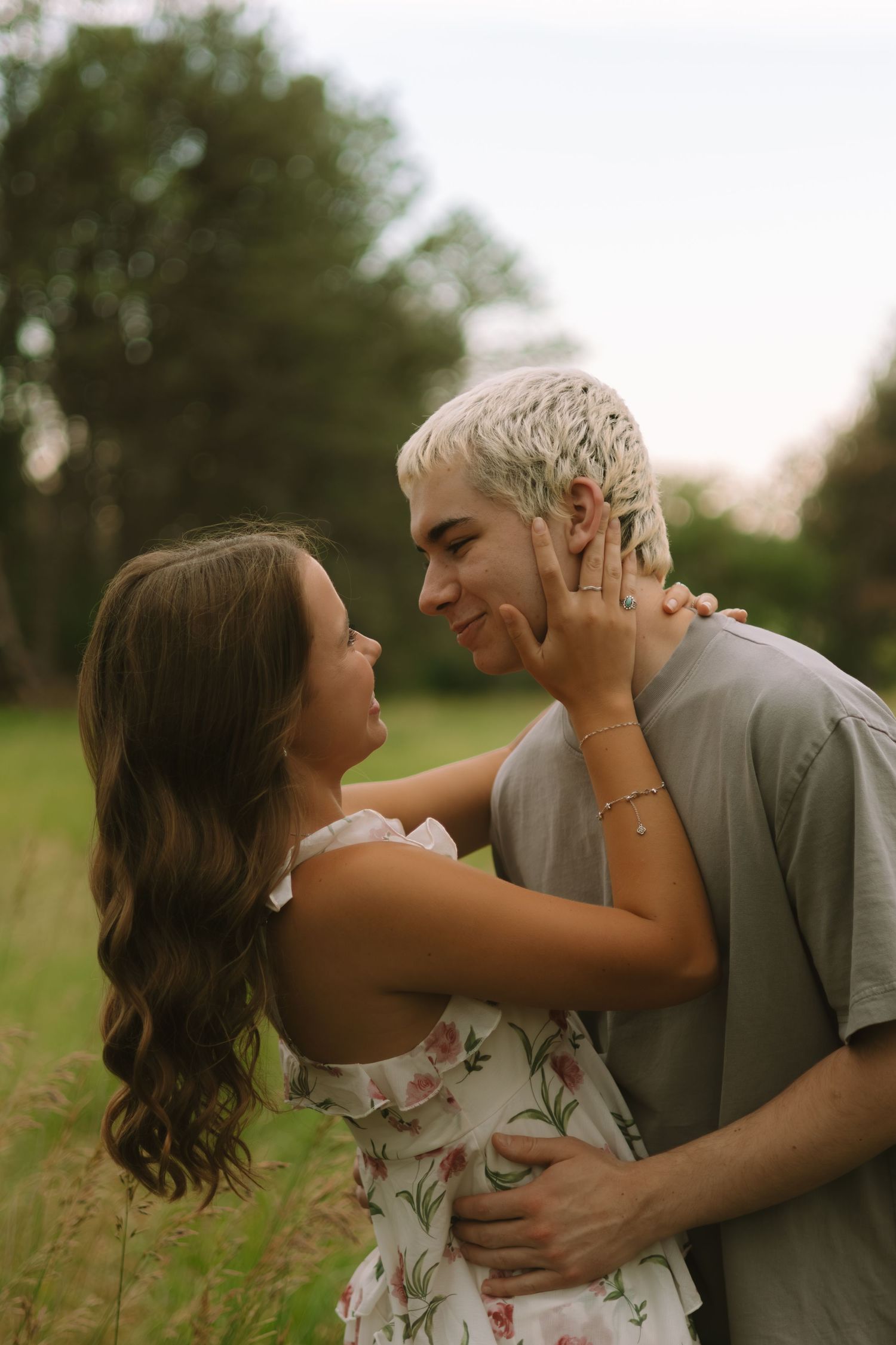 A tender moment between a couple in a floral dress and grey shirt standing in tall grass.