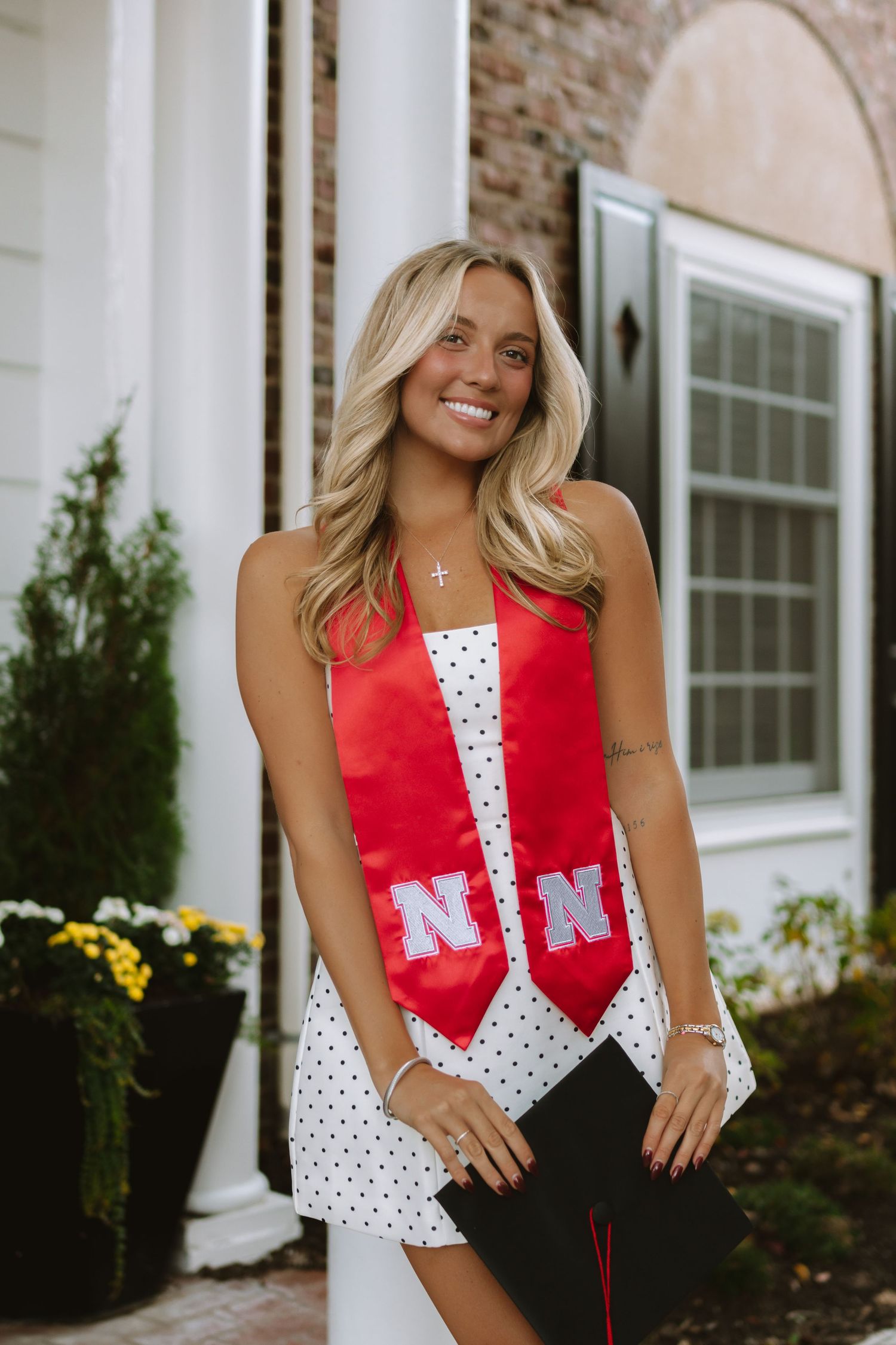 Graduate wearing Nebraska stole and polka dot dress poses outside brick building.