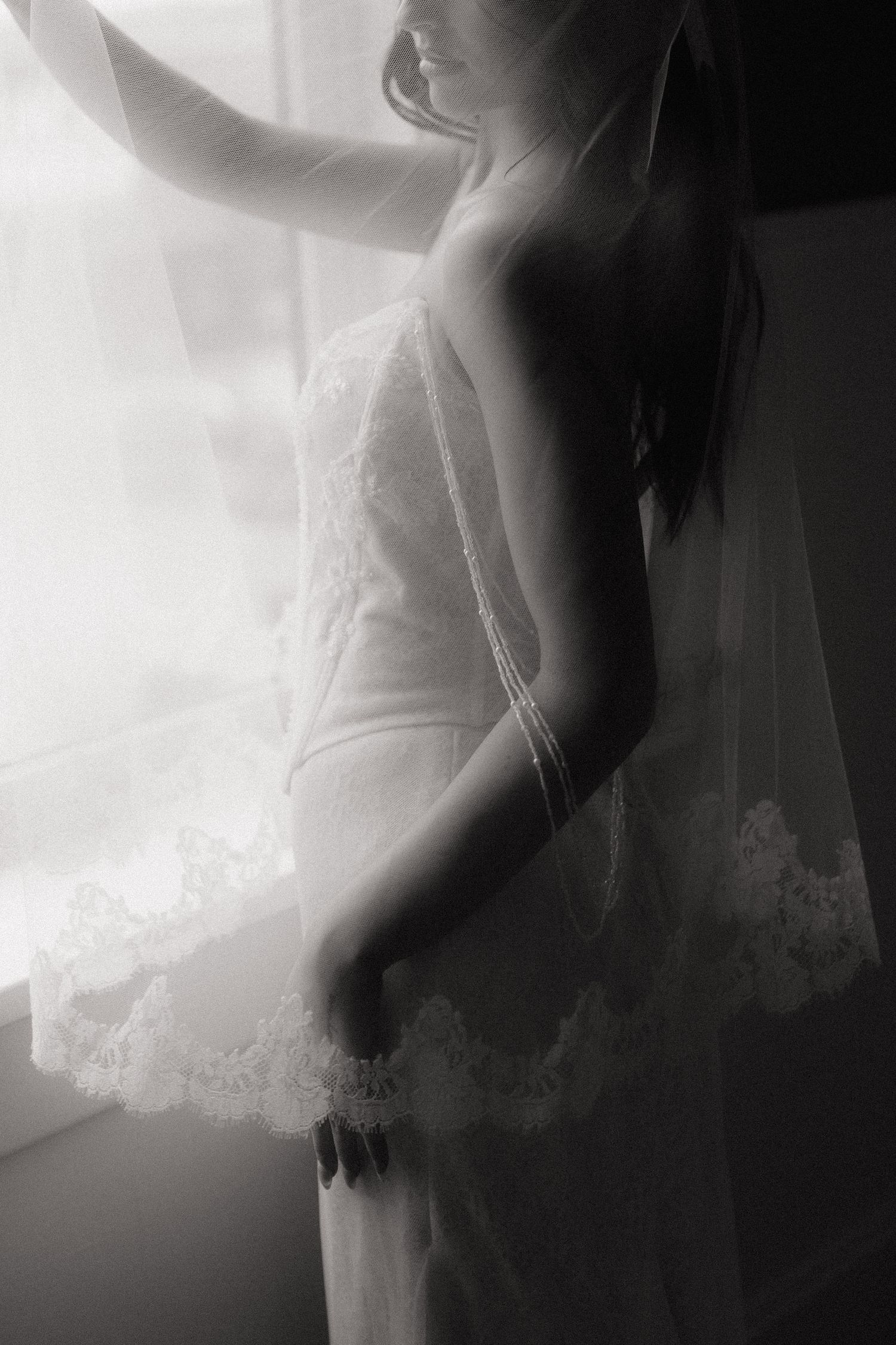 Artistic silhouette of bride in wedding dress against bright window.