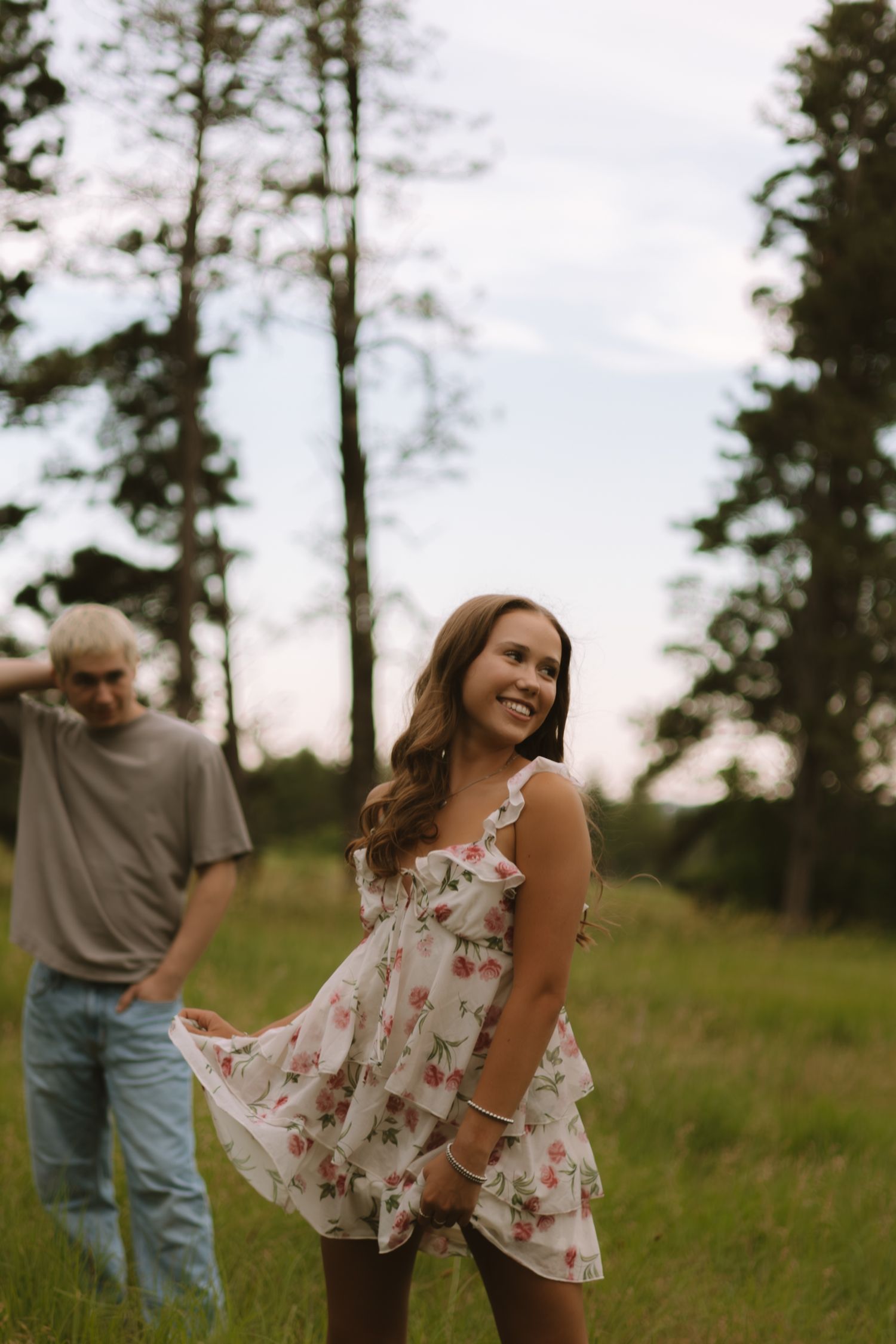A candid moment in a floral dress against a backdrop of tall pine trees during golden hour.