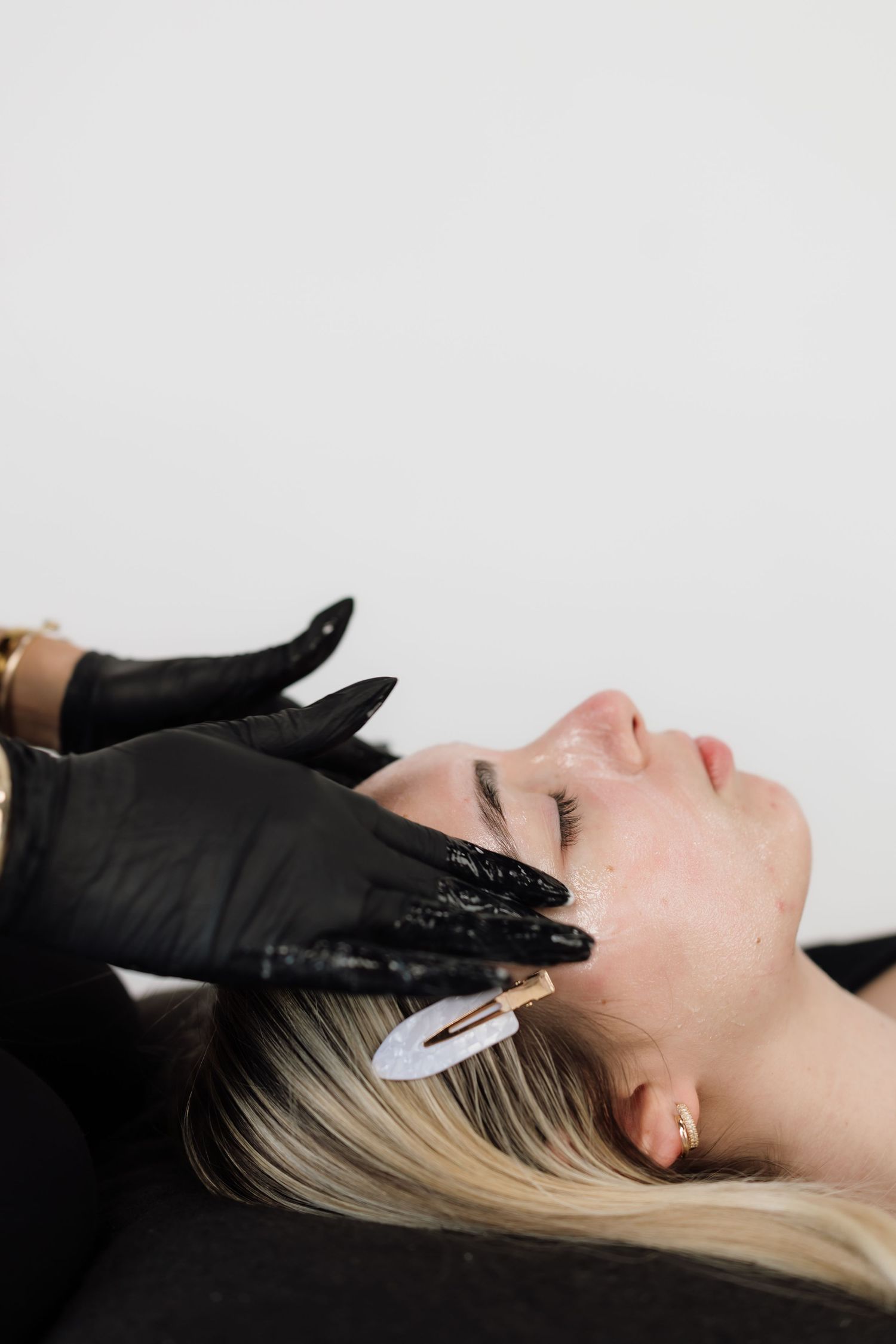 Minimalist beauty treatment photo showing hands in black gloves performing facial work.