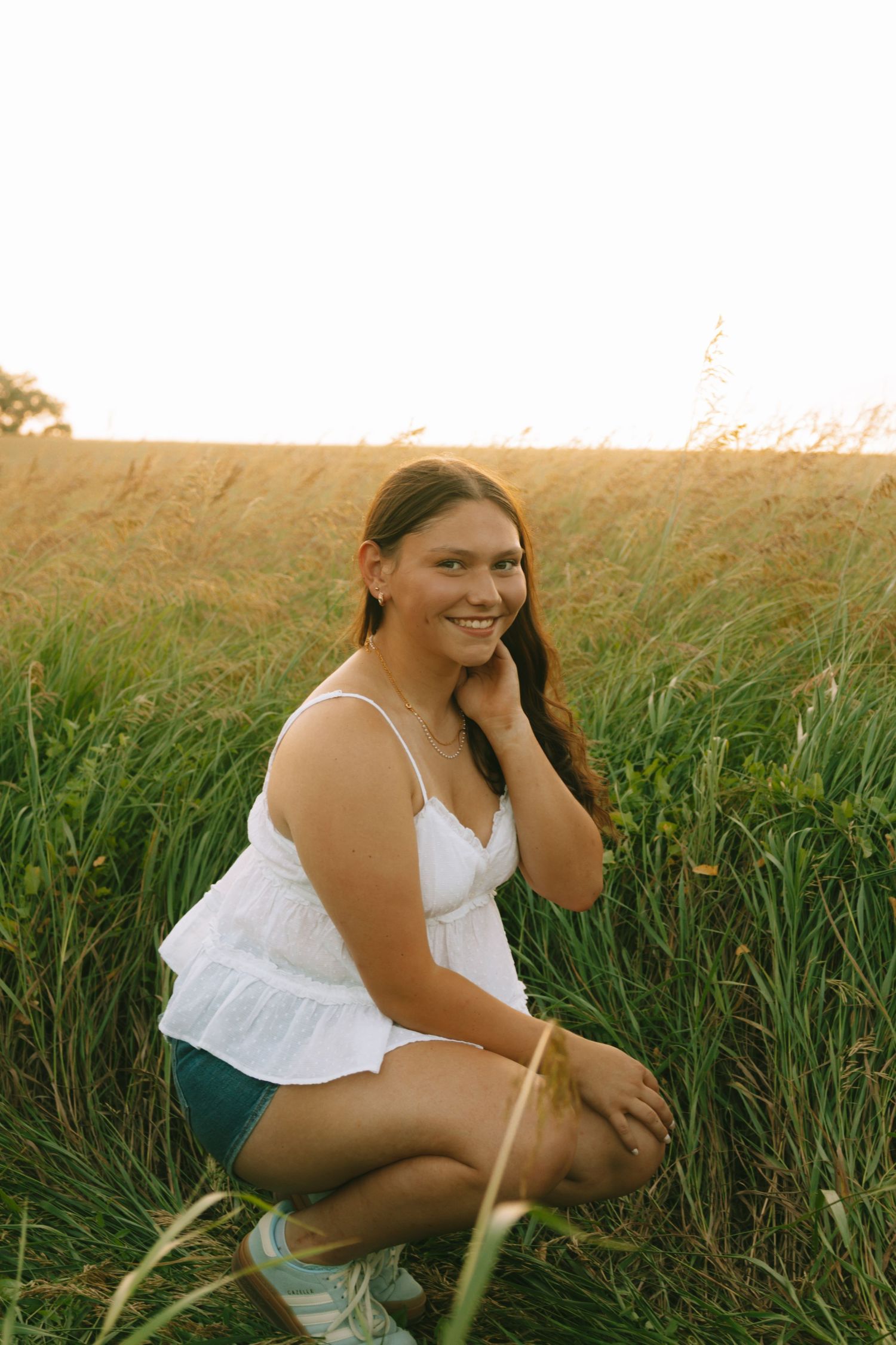 A person in white sits in tall grass during golden hour.