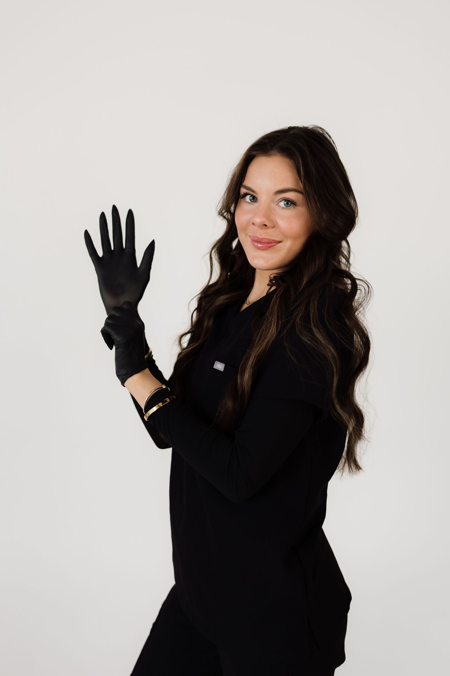 Person in all black outfit and gloves poses confidently against white background.