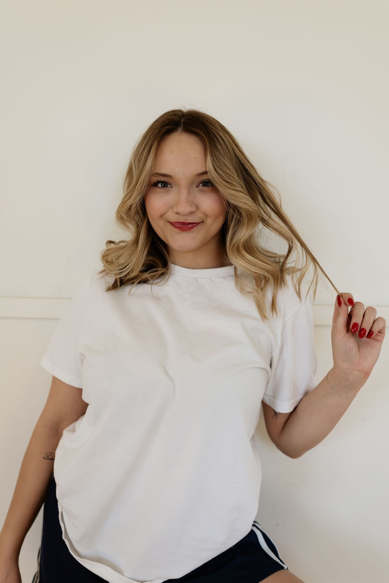 Casual portrait of someone wearing a white t-shirt and styled blonde wavy hair against a neutral wall.