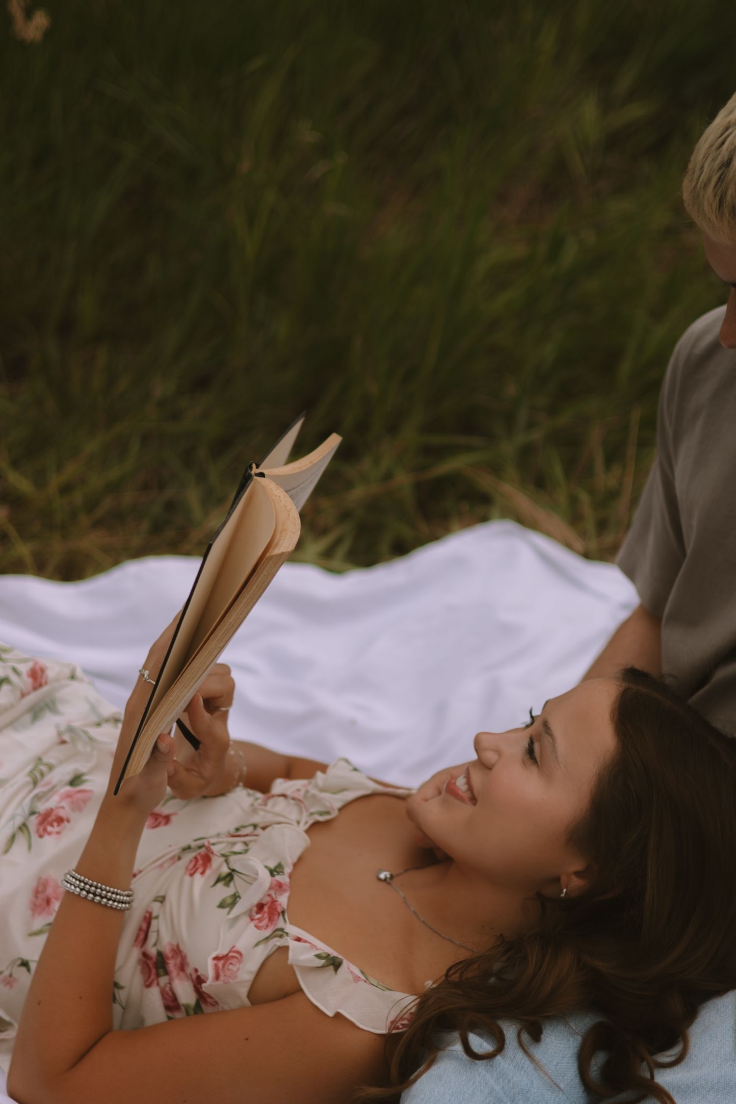 A romantic outdoor scene with a couple reading together on a white blanket surrounded by nature.