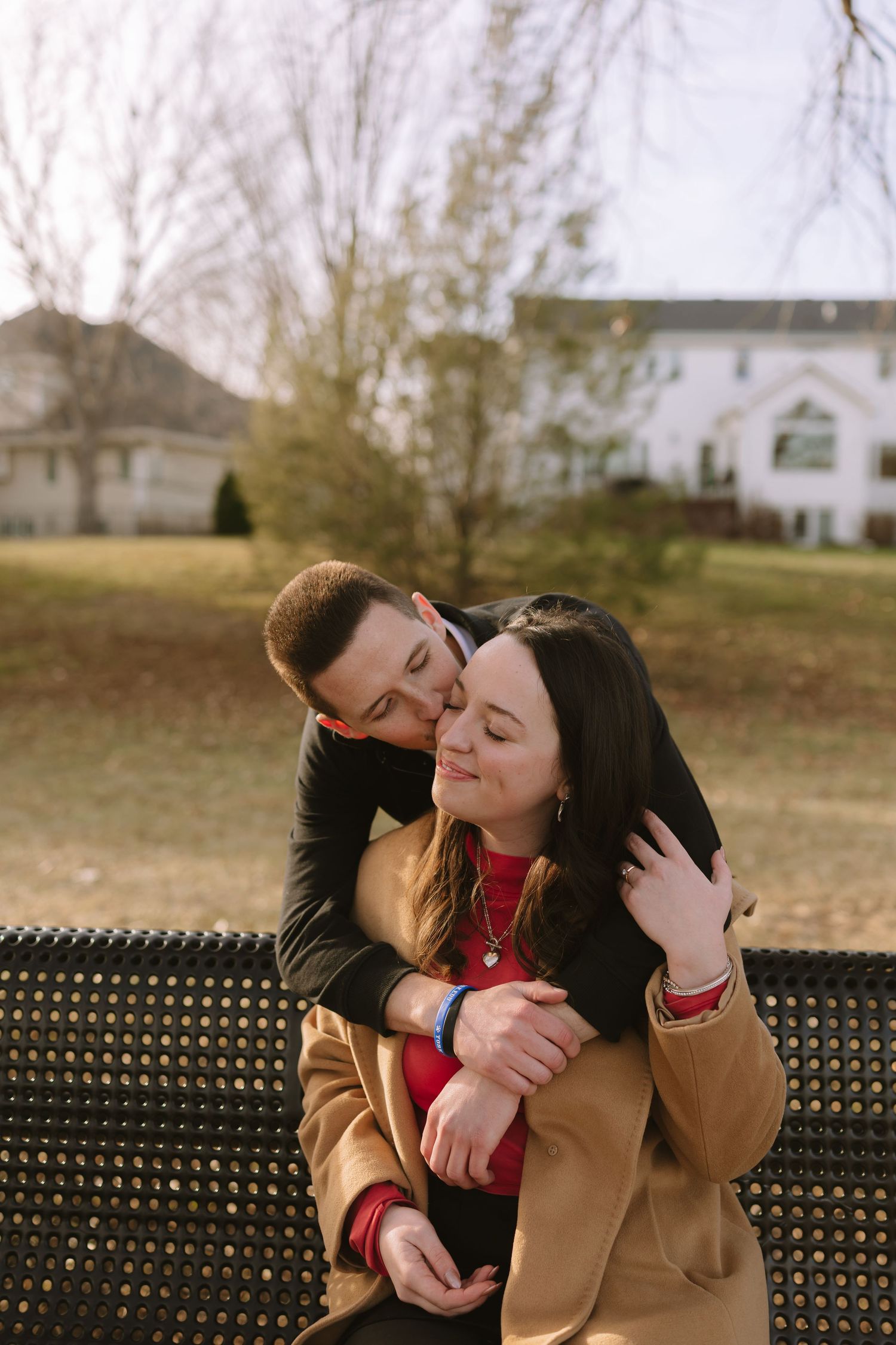 A couple shares an intimate embrace while sitting on a park bench.