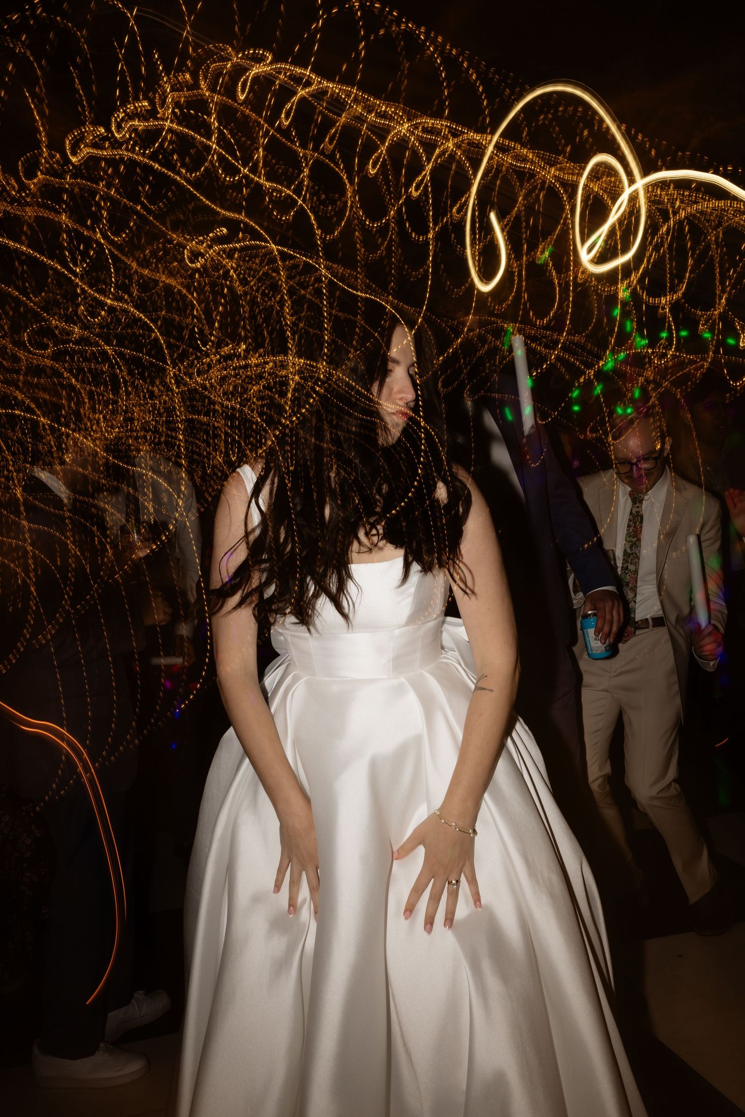 Bride in white satin ballgown dancing at wedding reception with light painting swirls in dark background.