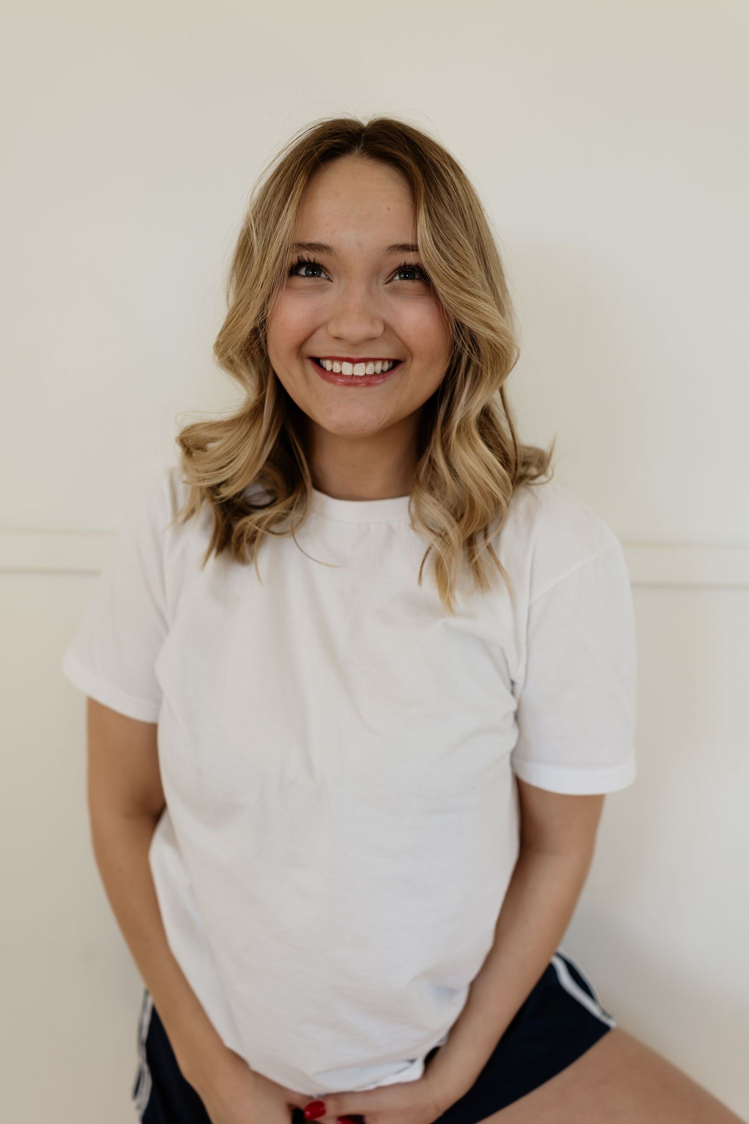 A person wearing a white t-shirt smiles while posing against a white wall in a series of casual photos.