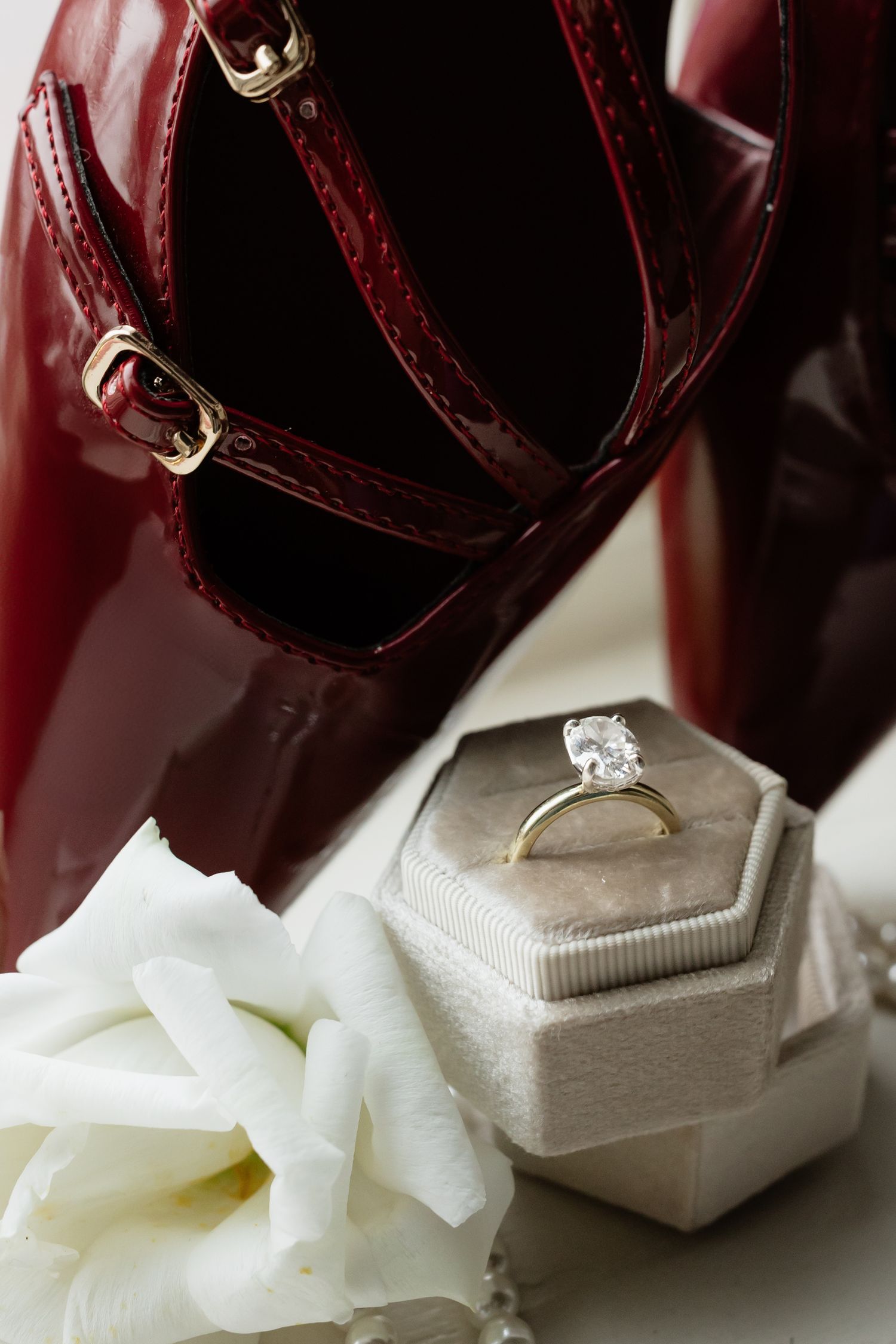 Diamond engagement ring nestled in white tissue paper with burgundy leather accessories in background.