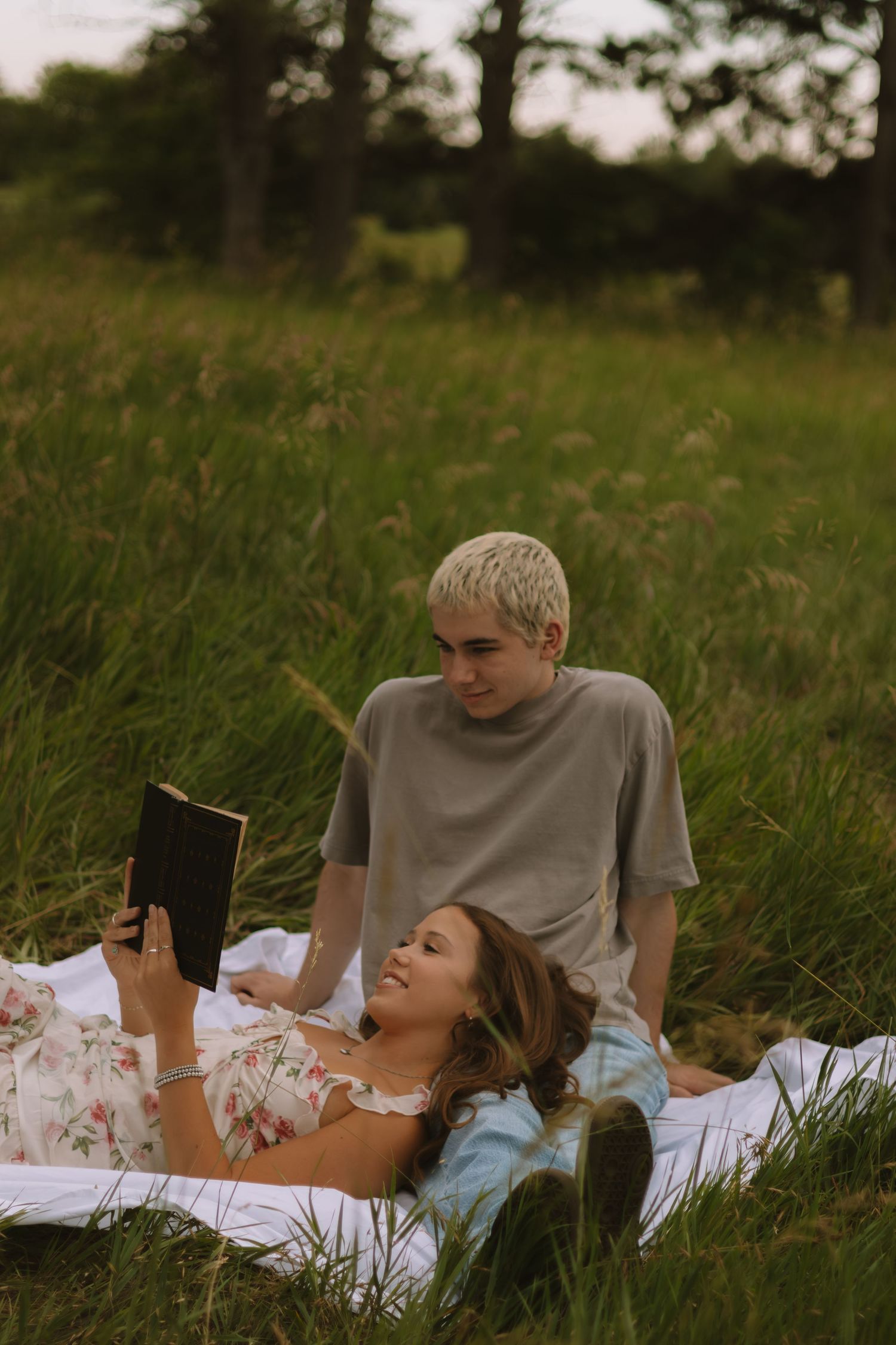 A couple relaxes on a blanket in a field while reading together.
