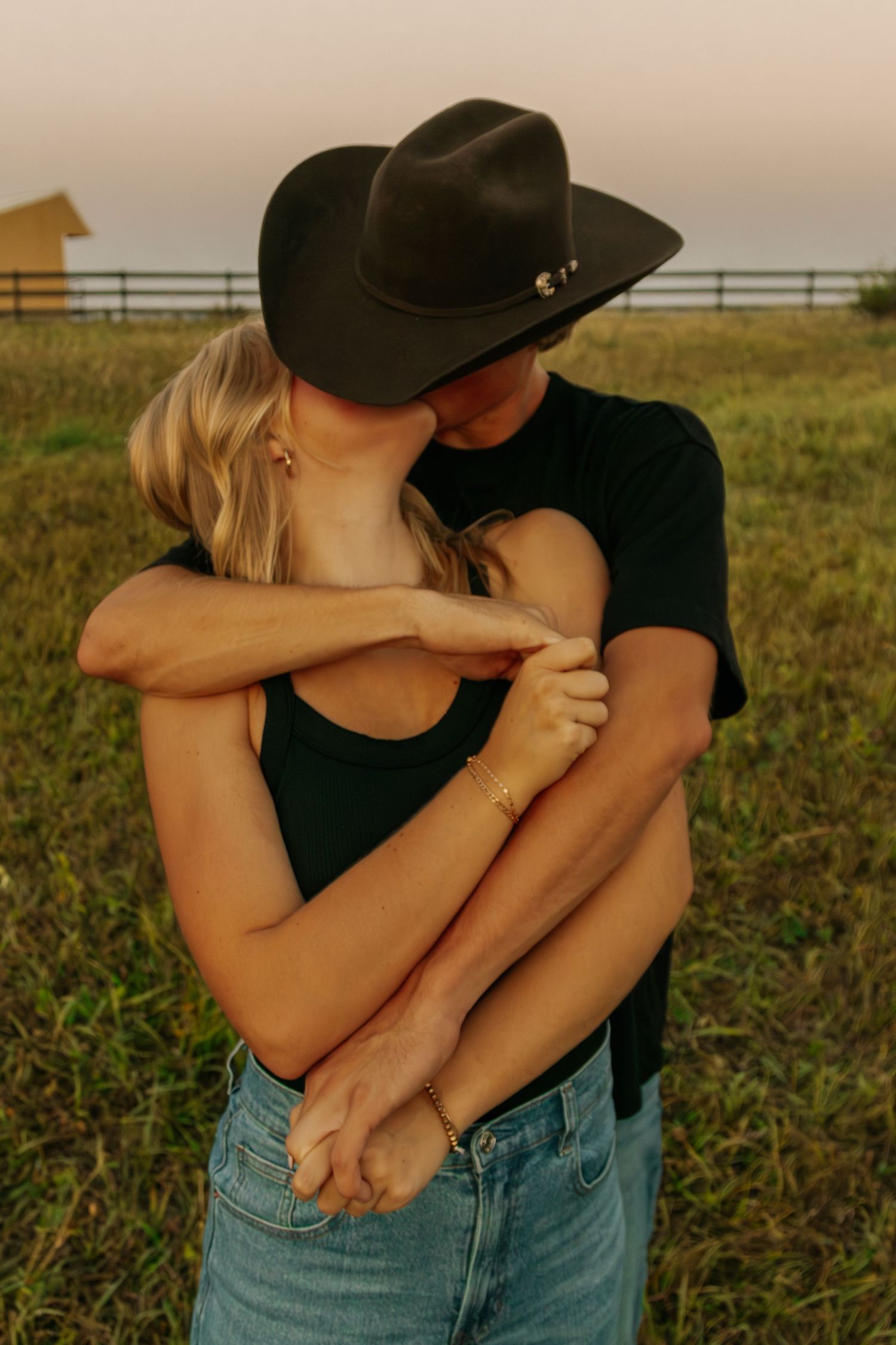 A couple in black tops and denim embracing in a rural setting.