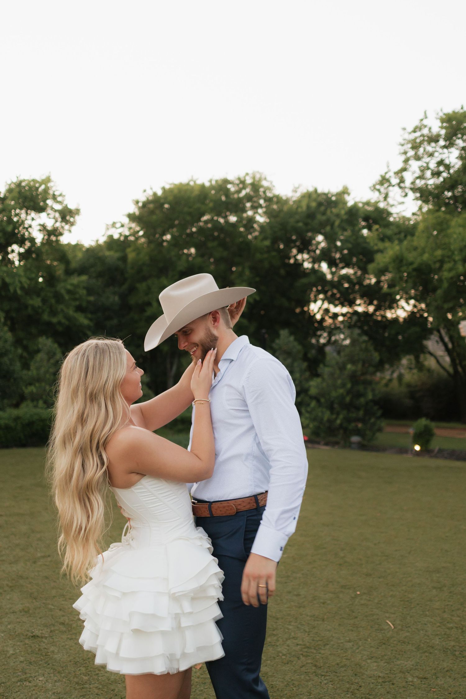 Intimate wedding portrait with bride and cowboy-styled groom on grassy field.